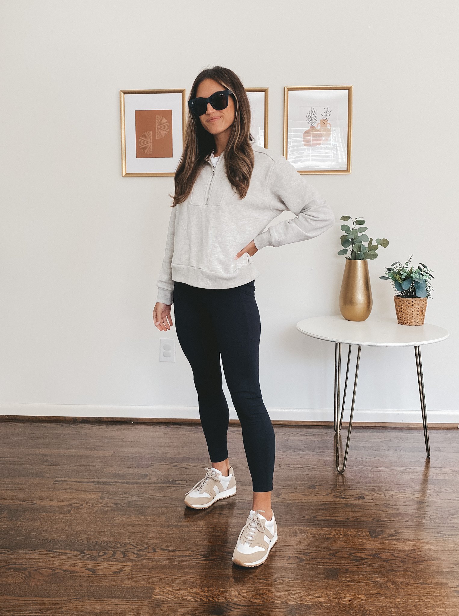 ashley wearing a gray track sweatshirt, black leggings, white and tan leather sneakers and black square frame sunglasses
