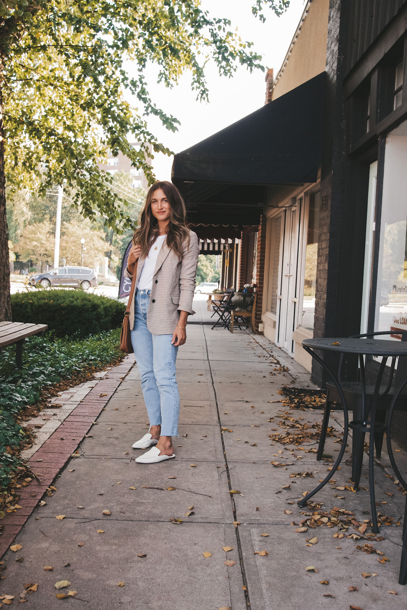 ashley standing on a sidewalk wearing a plaid blazer, white tee, light wash jeans, and white mules