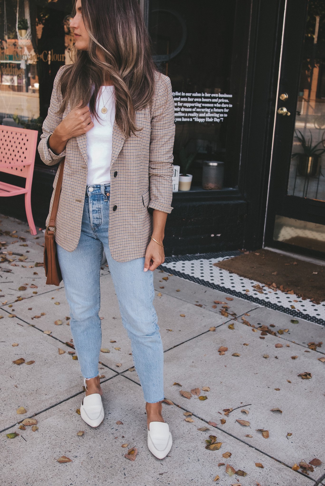 ashley standing on a sidewalk wearing a plaid blazer, white tee, light wash jeans, and white mules