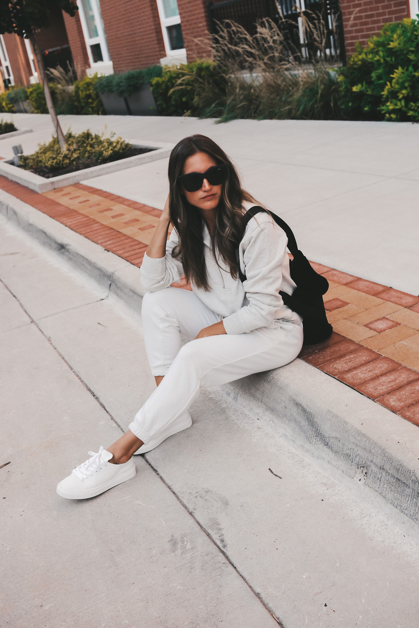 ashley sitting on a curb wearing a gray half zip sweatshirt, white joggers, and white sneakers