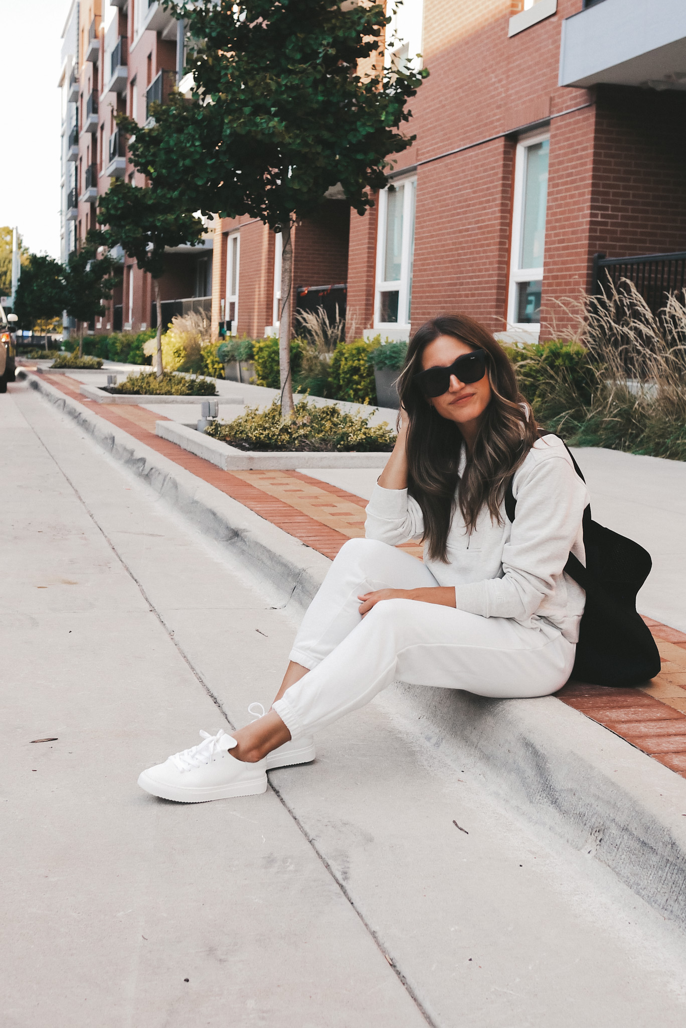 ashley sitting on a curb wearing a gray half zip sweatshirt, white joggers, and white sneakers