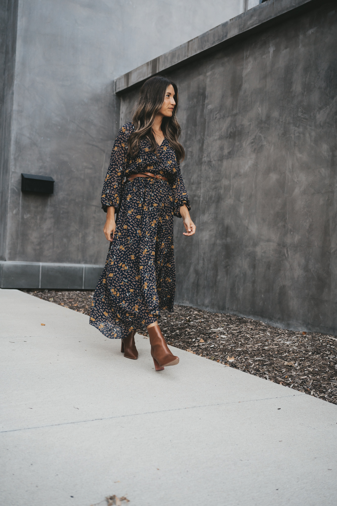 ashley walking down a sidewalk wearing a navy floral midi dress belted at the waist and brown ankle boots