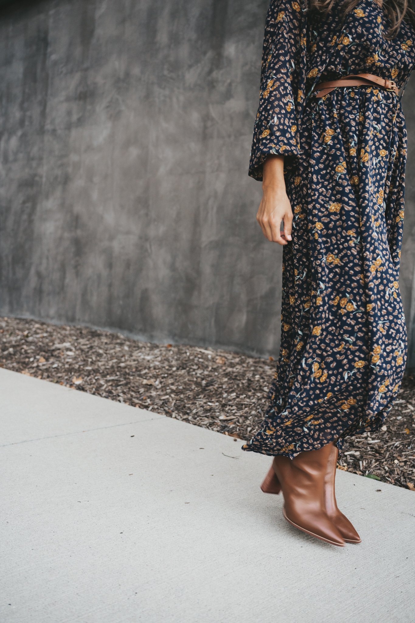 ashley wearing a navy blue floral midi skirt with a skinny belt at the waist and cognac ankle boots