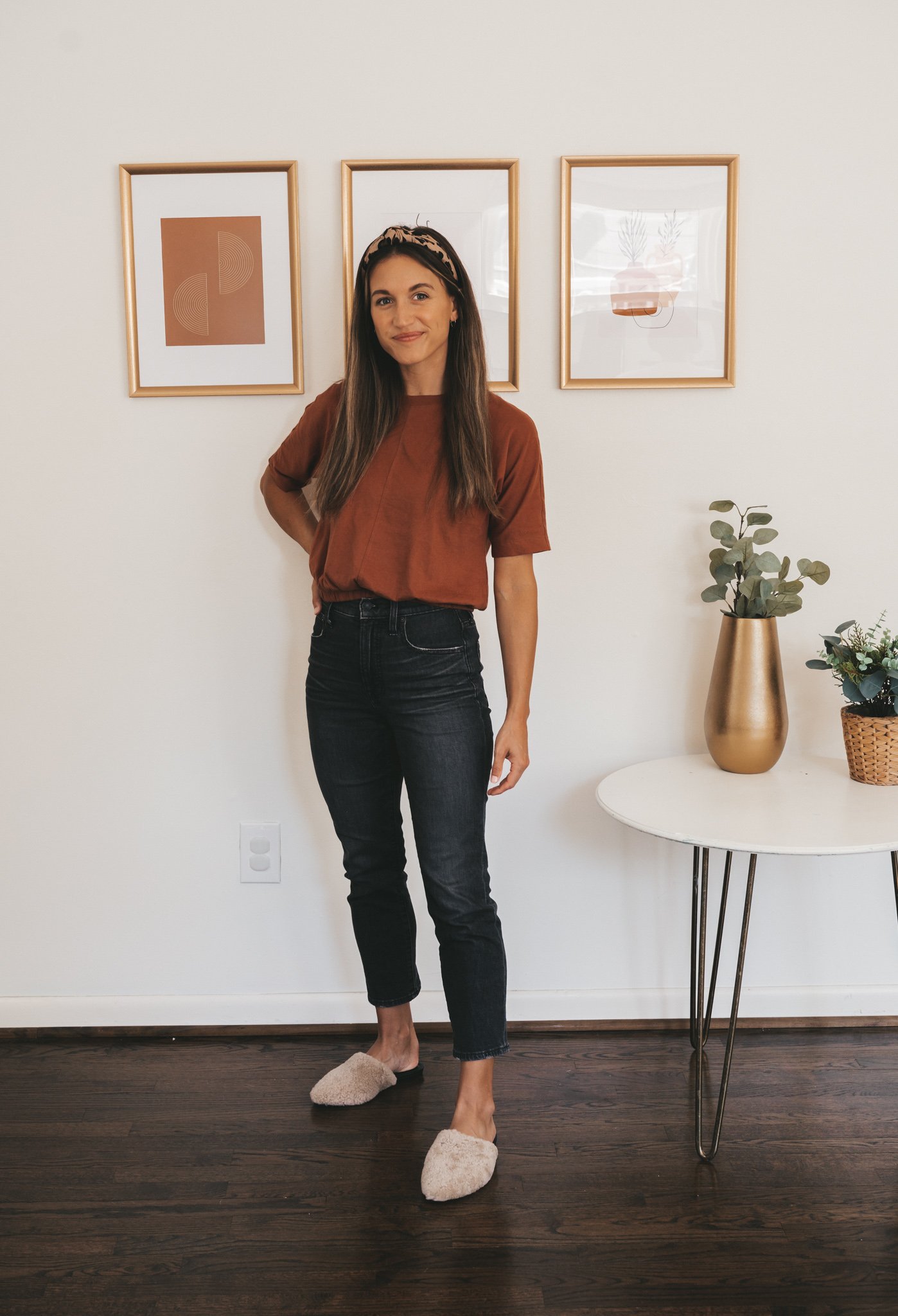 ashley wearing a rust colored tee, washed black jeans, tan shearling mules and a leopard print headband