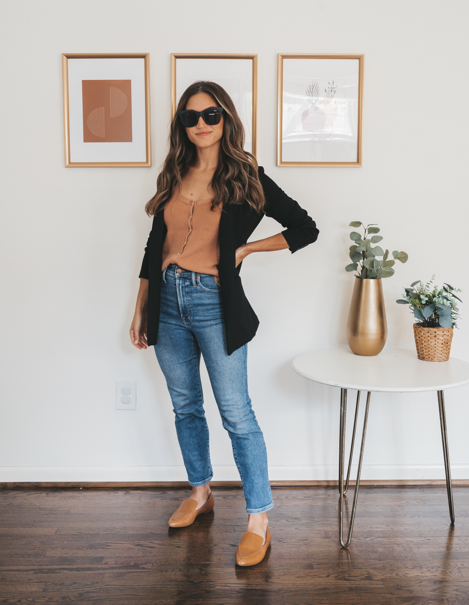 ashley wearing a tan button front sweater tank, black blazer, medium wash denim, and cognac loafers