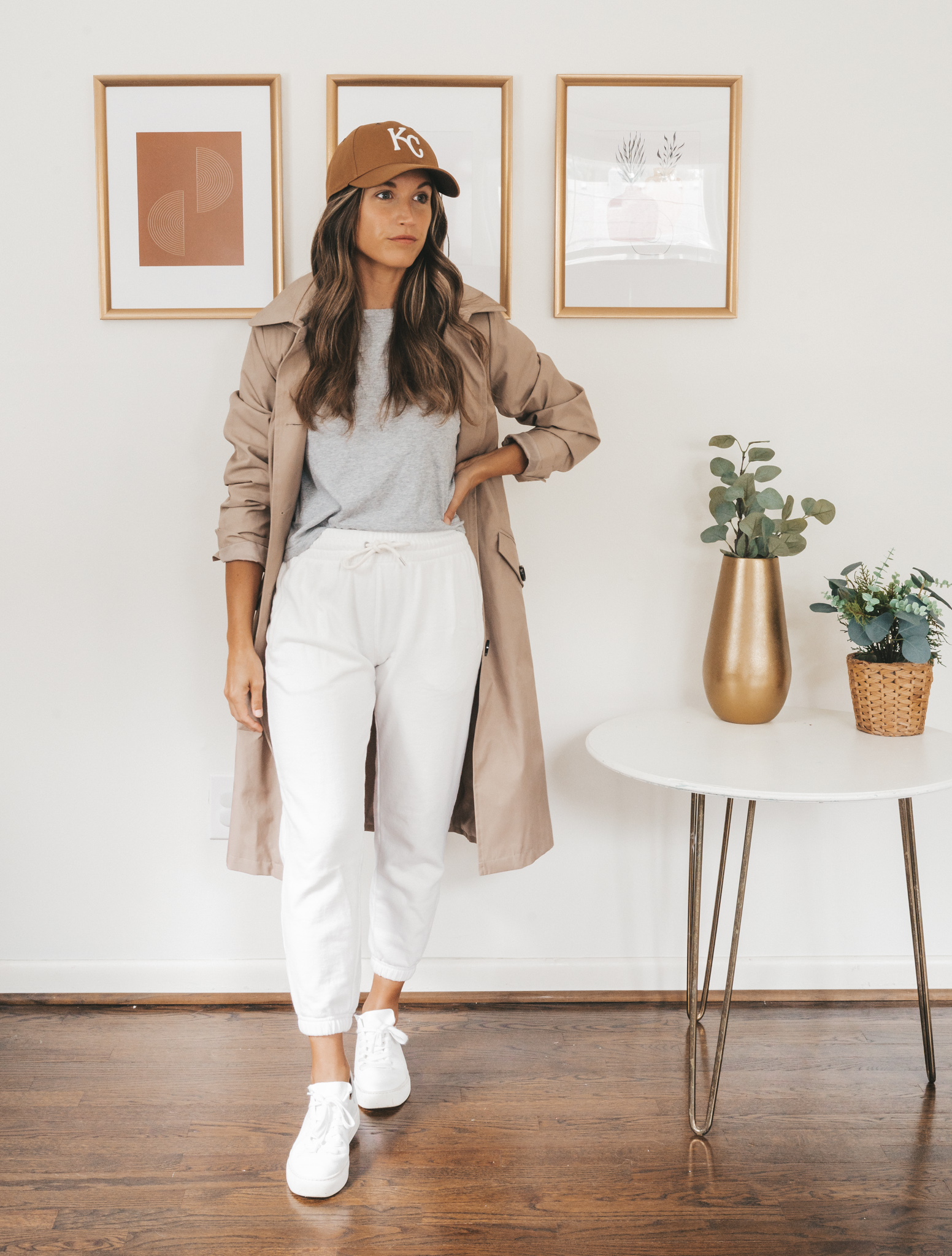 ashley wearing a gray tee, white joggers, taupe trench coat, white sneakers and a Carhartt brown KC baseball hat