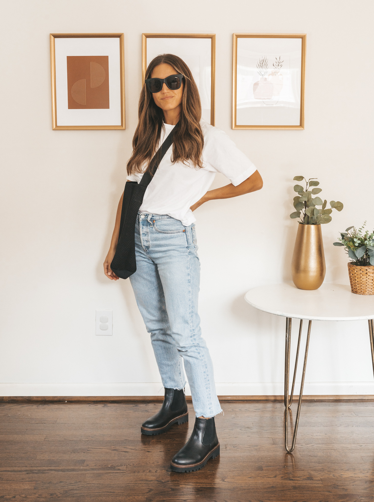 ashley wearing a white tee, light wash straight leg jeans, black lug sole Chelsea boots, and a black mesh tote bag