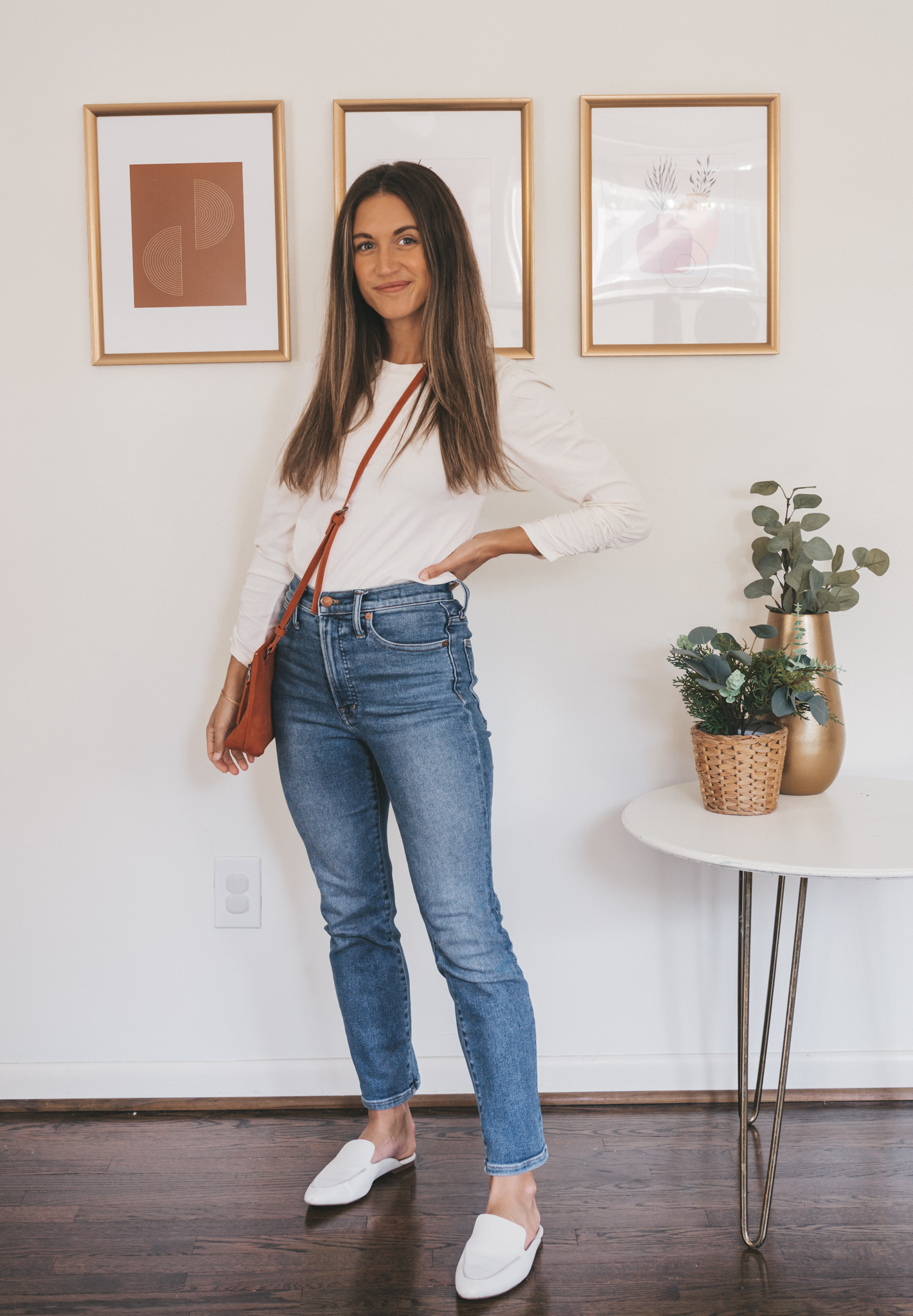 ashley wearing a white puff sleeve tee, medium wash denim, white mules and a dark orange crossbody bag
