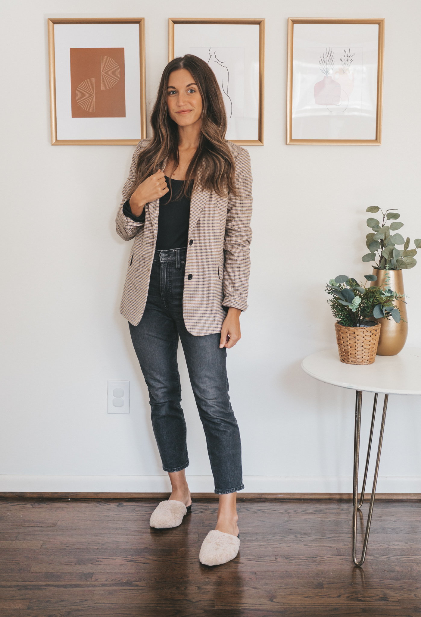 ashley wearing a black bodysuit, plaid blazer, washed black jeans, and tan shearling mules