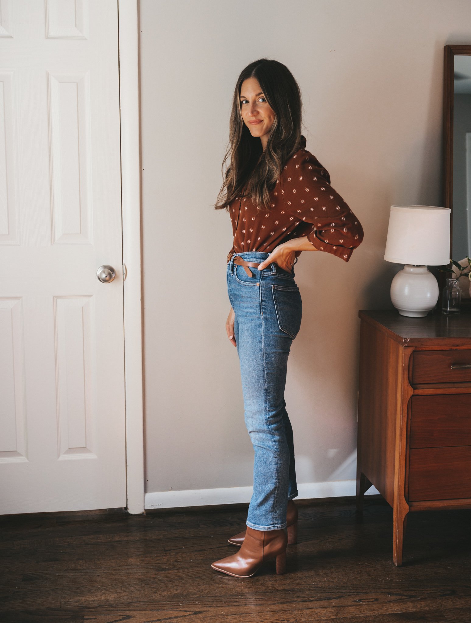 ashley wearing a rust colored patterned peasant blouse, medium wash mom jeans, and cognac ankle boots