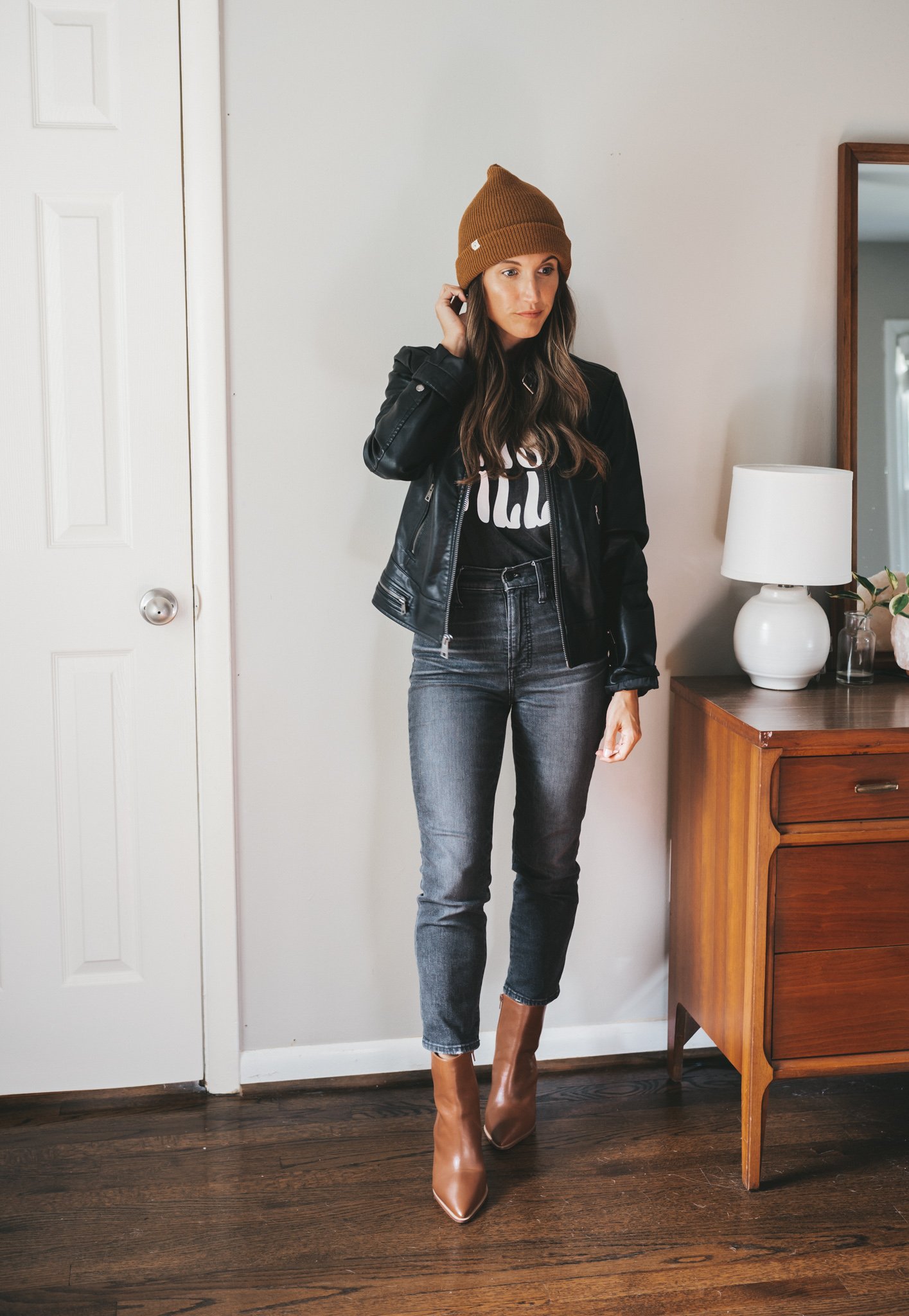 ashley wearing a faux leather moto jacket, washed black graphic tee with the words Nashville, washed black denim, cognac ankle boots and a brown beanie