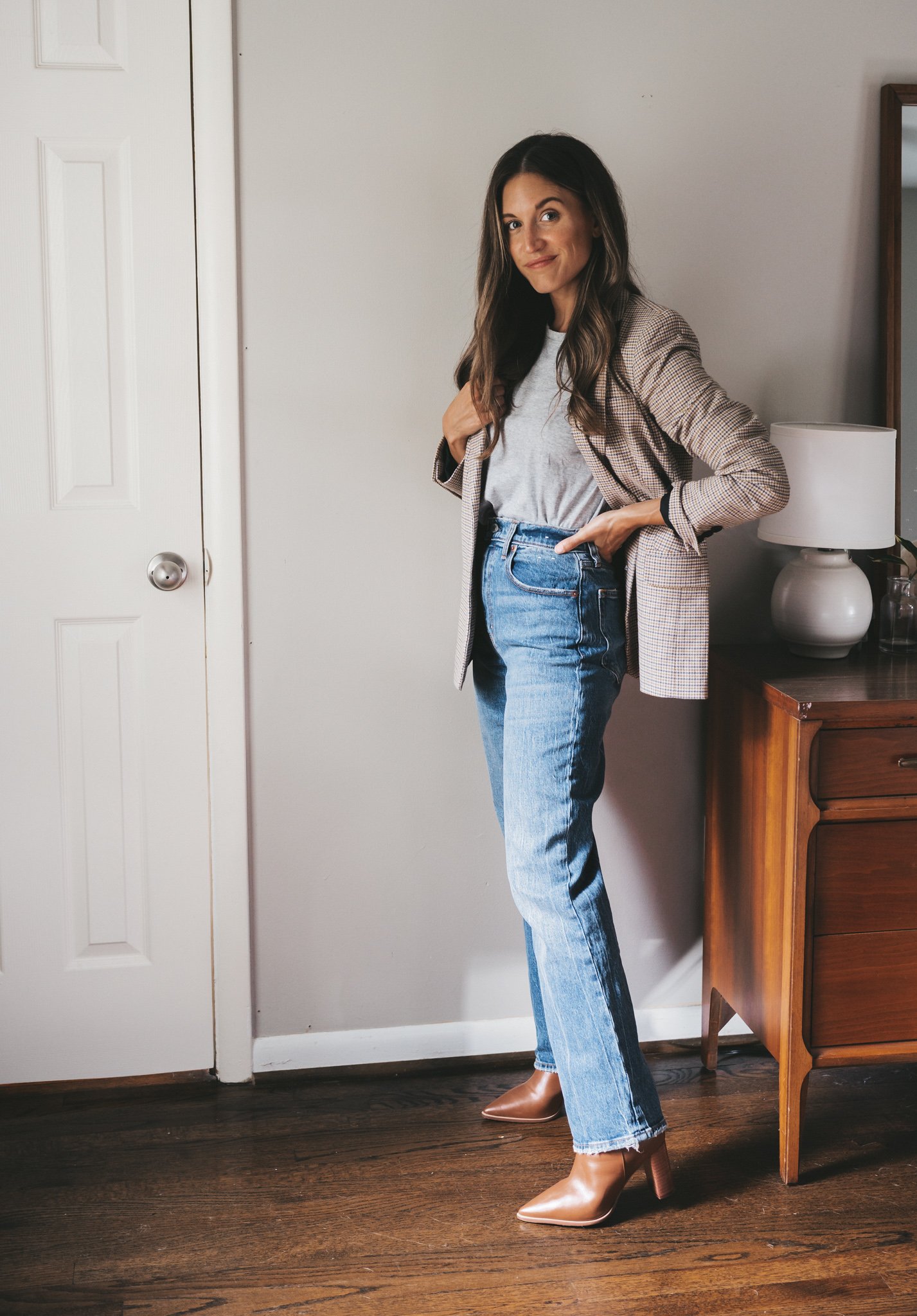 ashley wearing a plaid blazer, gray tee, and full length medium wash straight leg jeans, with cognac ankle boots
