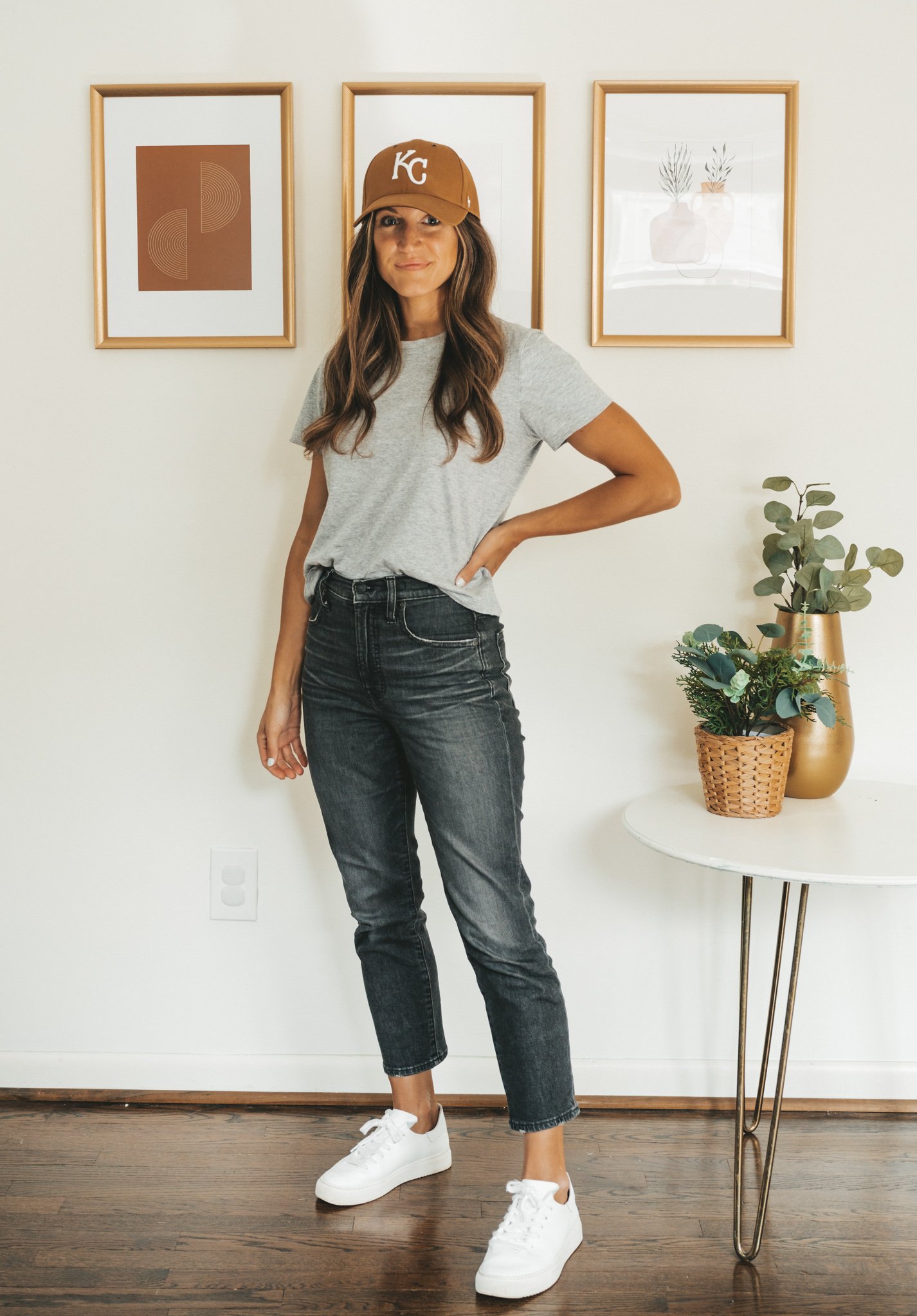 ashley wearing a gray tee, washed black jeans, white sneakers and a Carhartt brown KC baseball hat