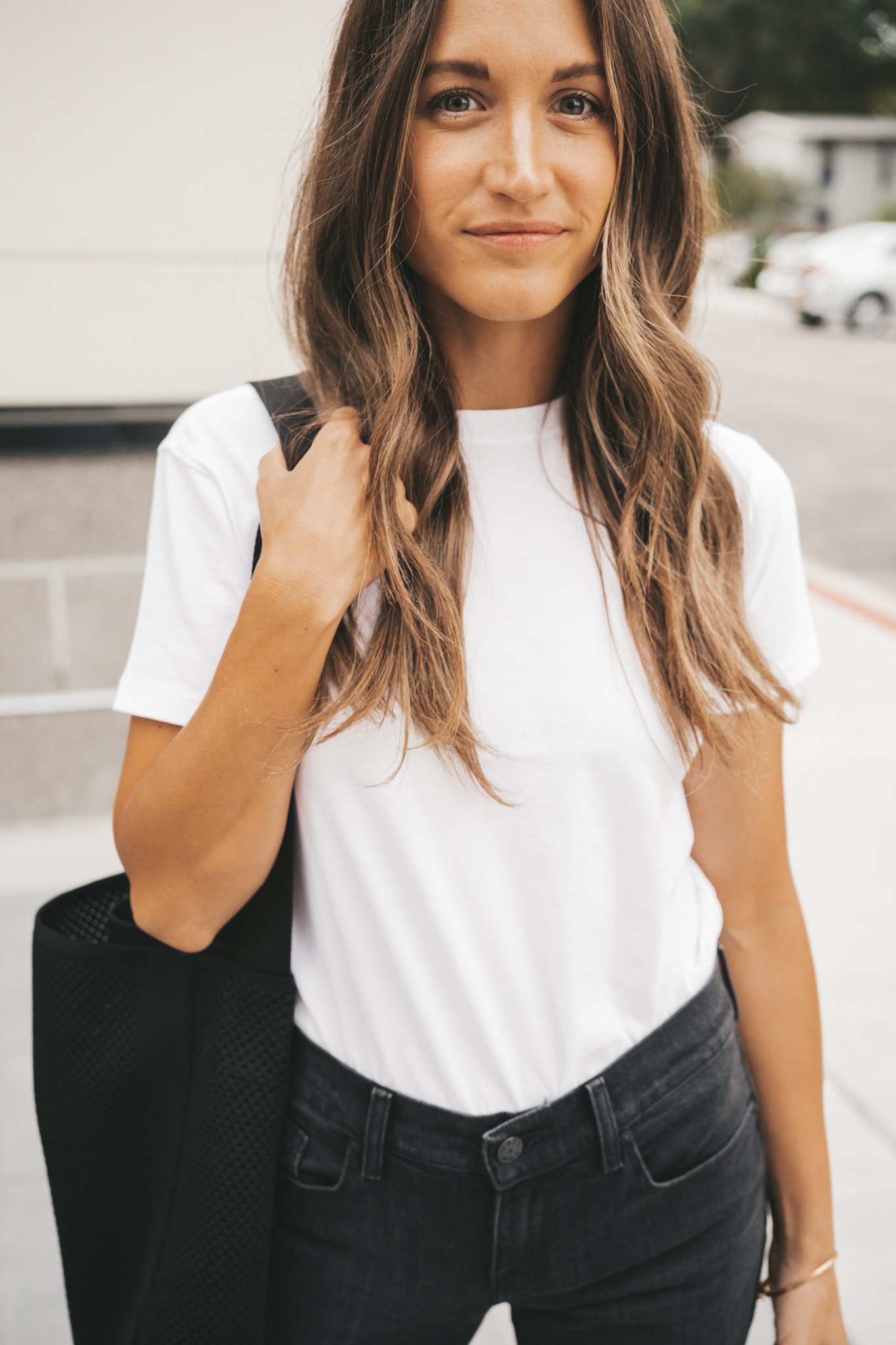 ashley wearing a white tee and black denim from Mott and Bow with a black tote bag standing on a sidewalk next to a white and gray building