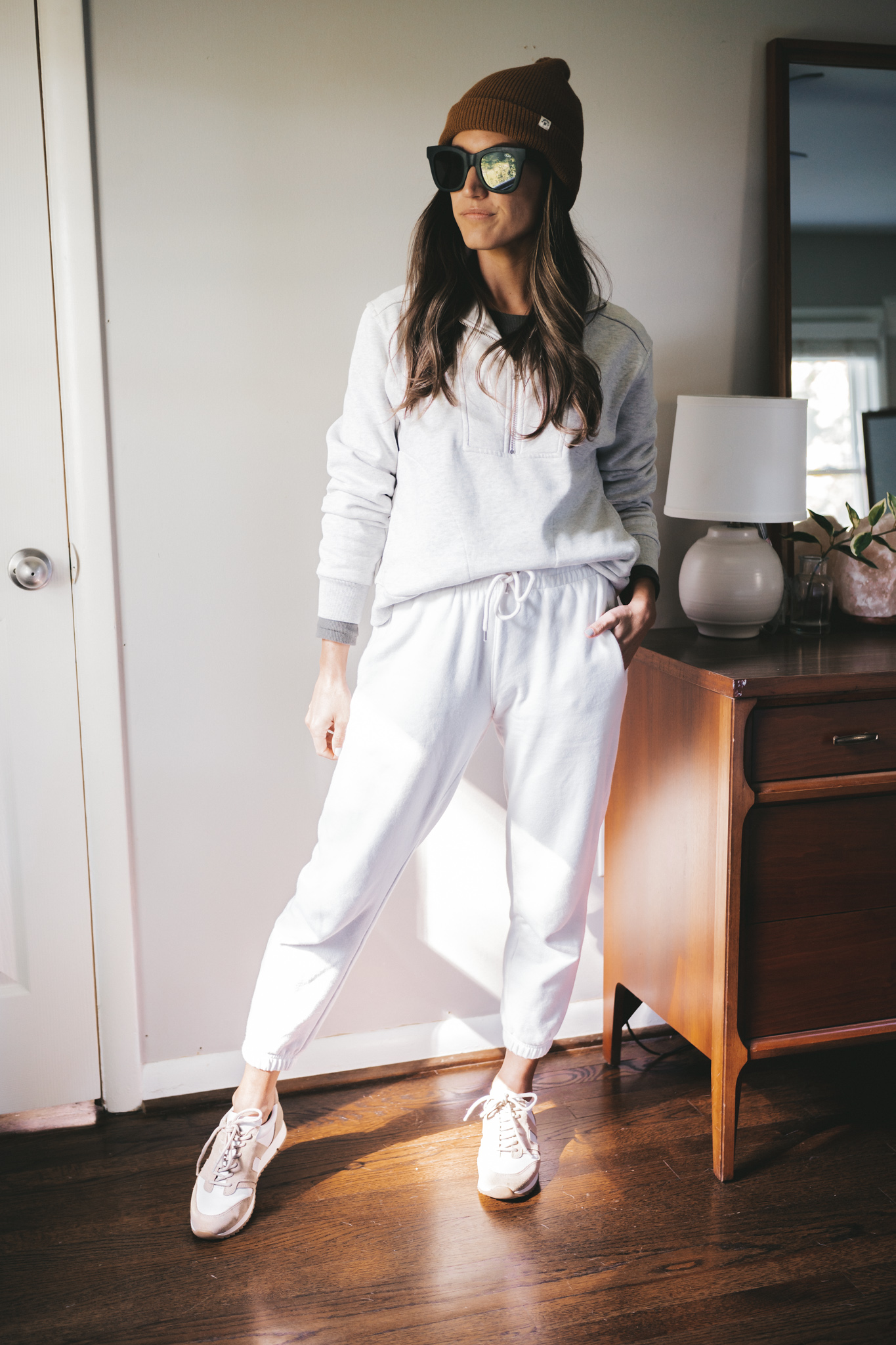 ashley wearing a gray half zip sweathshirt, white joggers, white and tan sneakers and a brown beanie
