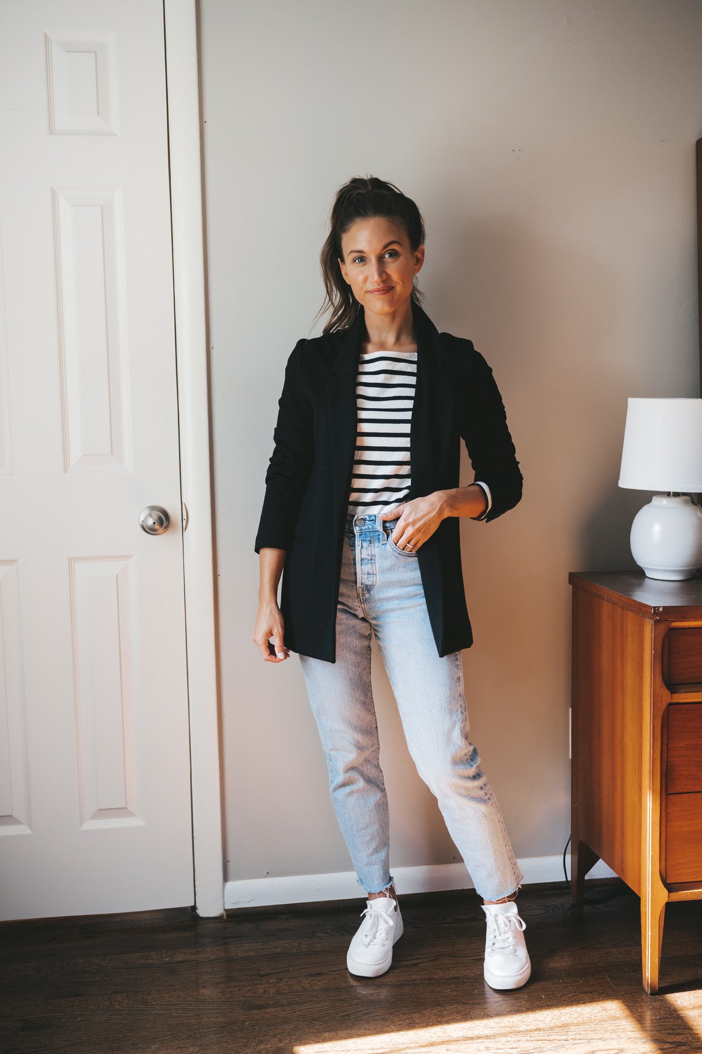 ashley wearing a black and white striped top, black blazer, light wash mom jeans, and white sneakers
