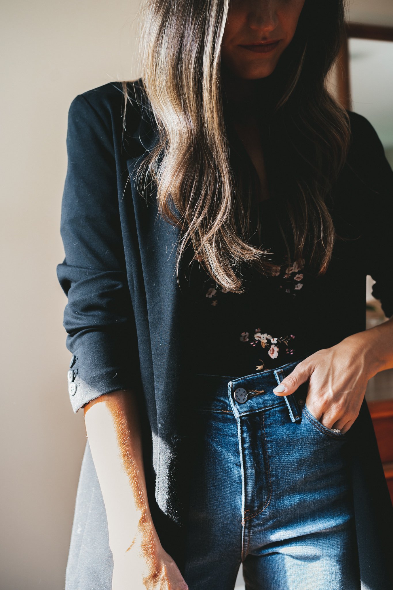 a close up shot of ashley wearing a black floral top, black blazer, and medium wash denim