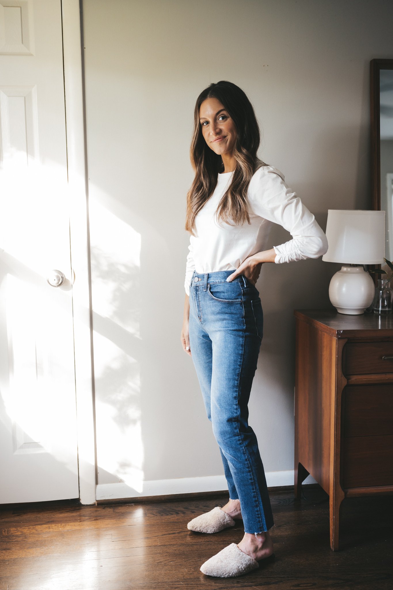 ashley wearing a white puff sleeve top, medium wash mom jeans, and tan shearling mules 