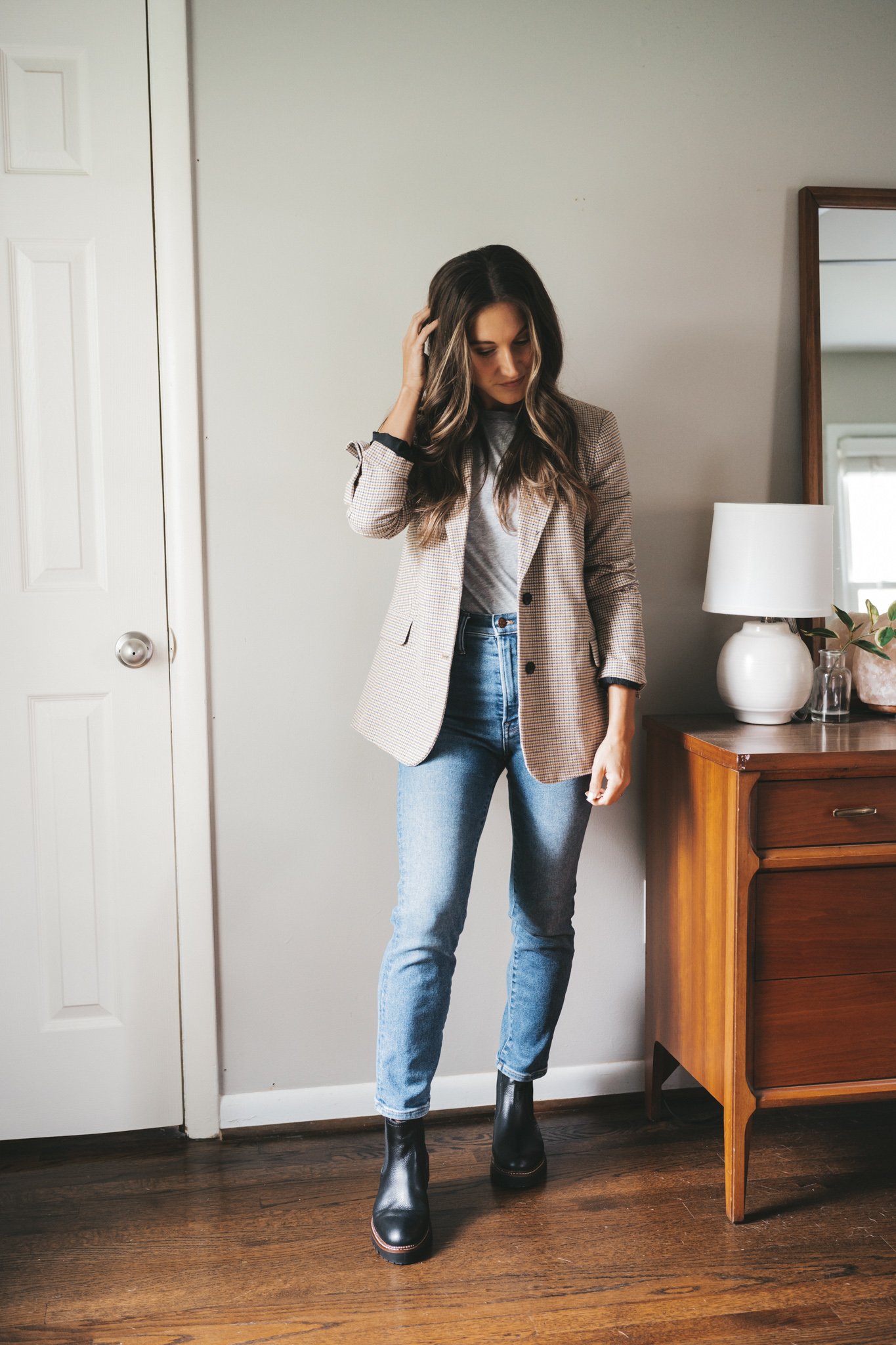 ashley wearing a long-sleeved gray tee, plaid blazer, medium wash mom jeans, and black lug sole Chelsea boots