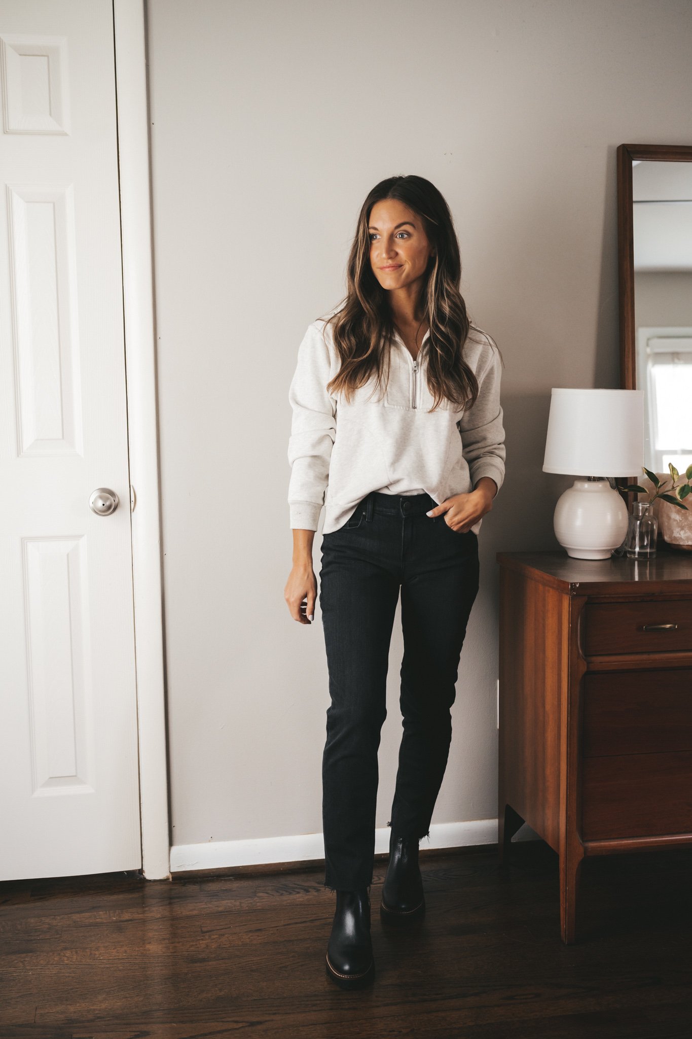 ashley wearing a light gray half-zip sweatshirt, black boyfriend jeans, and black lug sole chelsea boots