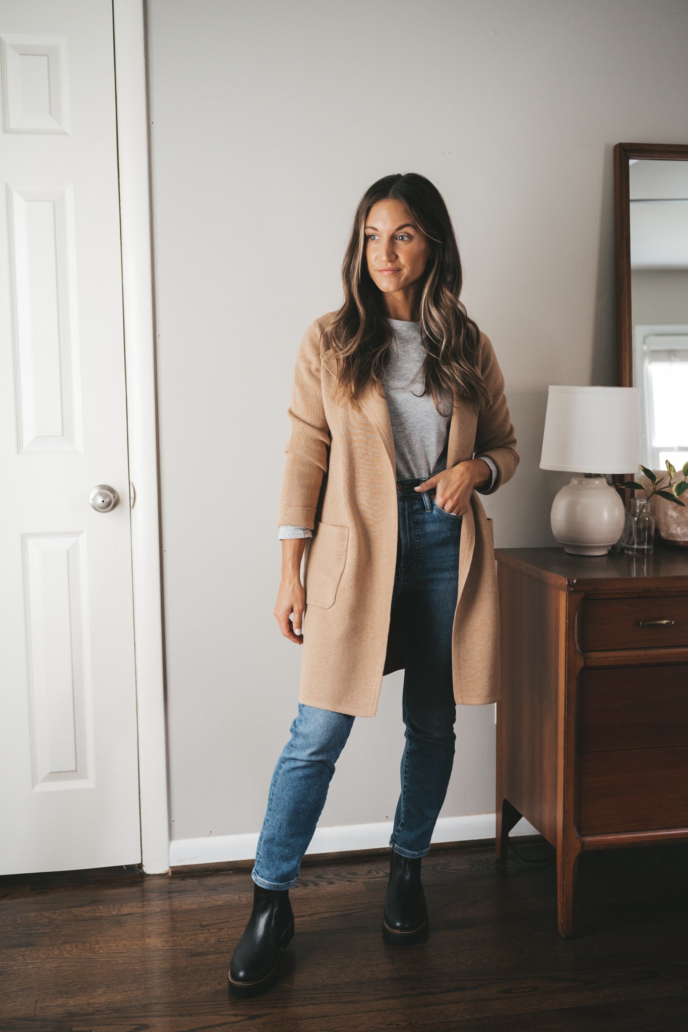 ashley wearing a gray tee under a tan coatigan, mid-wash mom jeans, and black lug sole chelsea boots