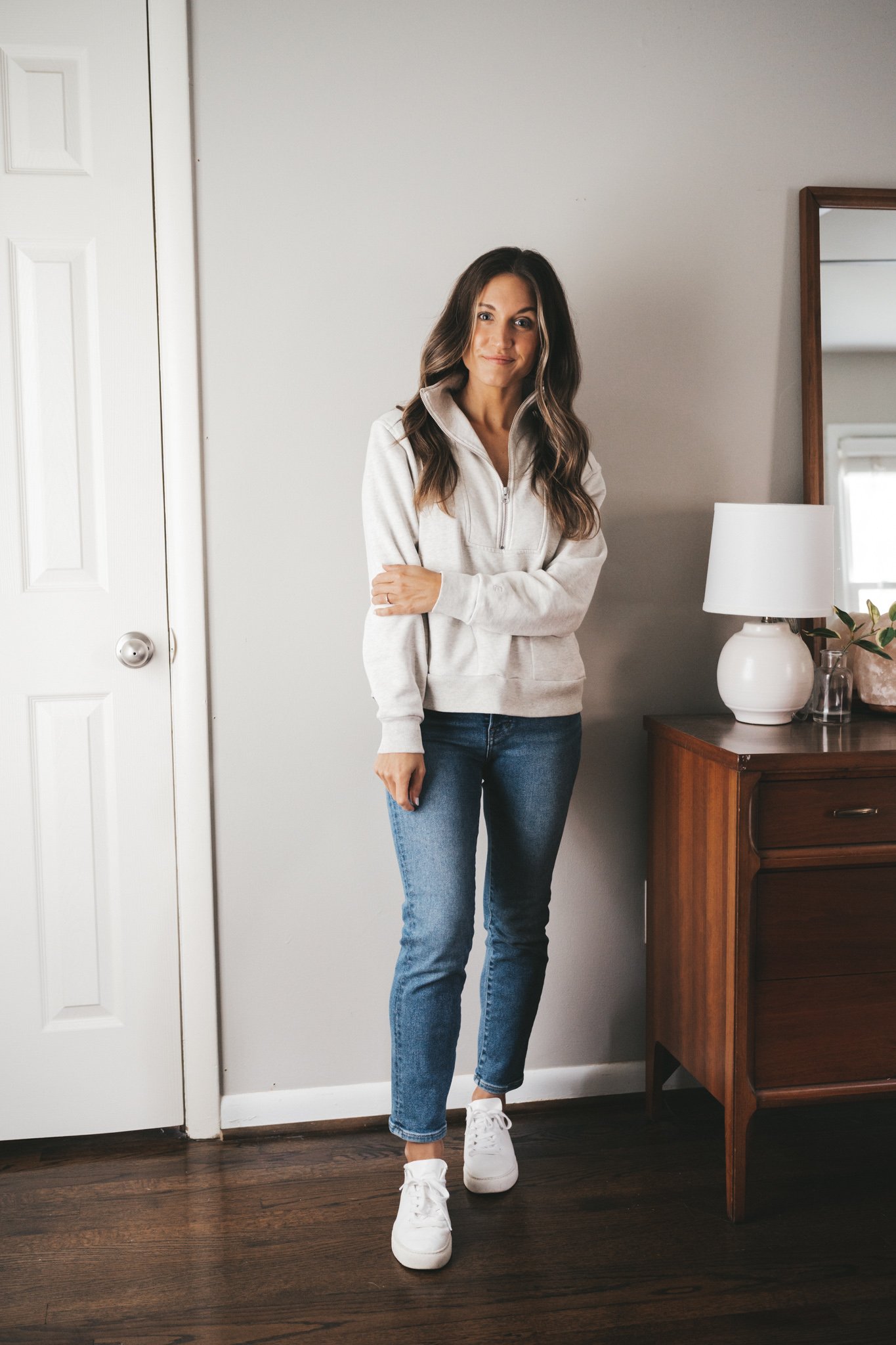 ashley wearing a gray half-zip sweatshirt, mid-wash mom jeans, and white sneakers