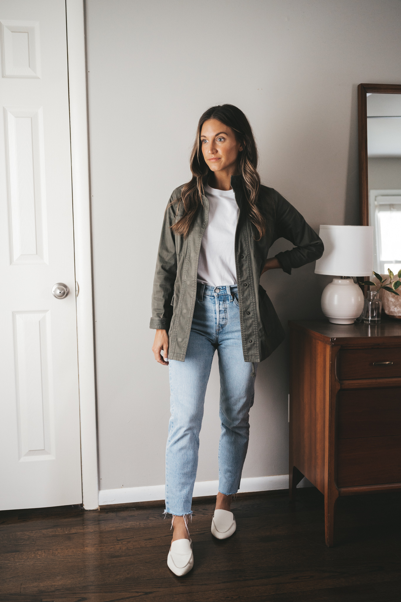 ashley wearing a white tee under a green utility jacket, light wash mom jeans, and white mules