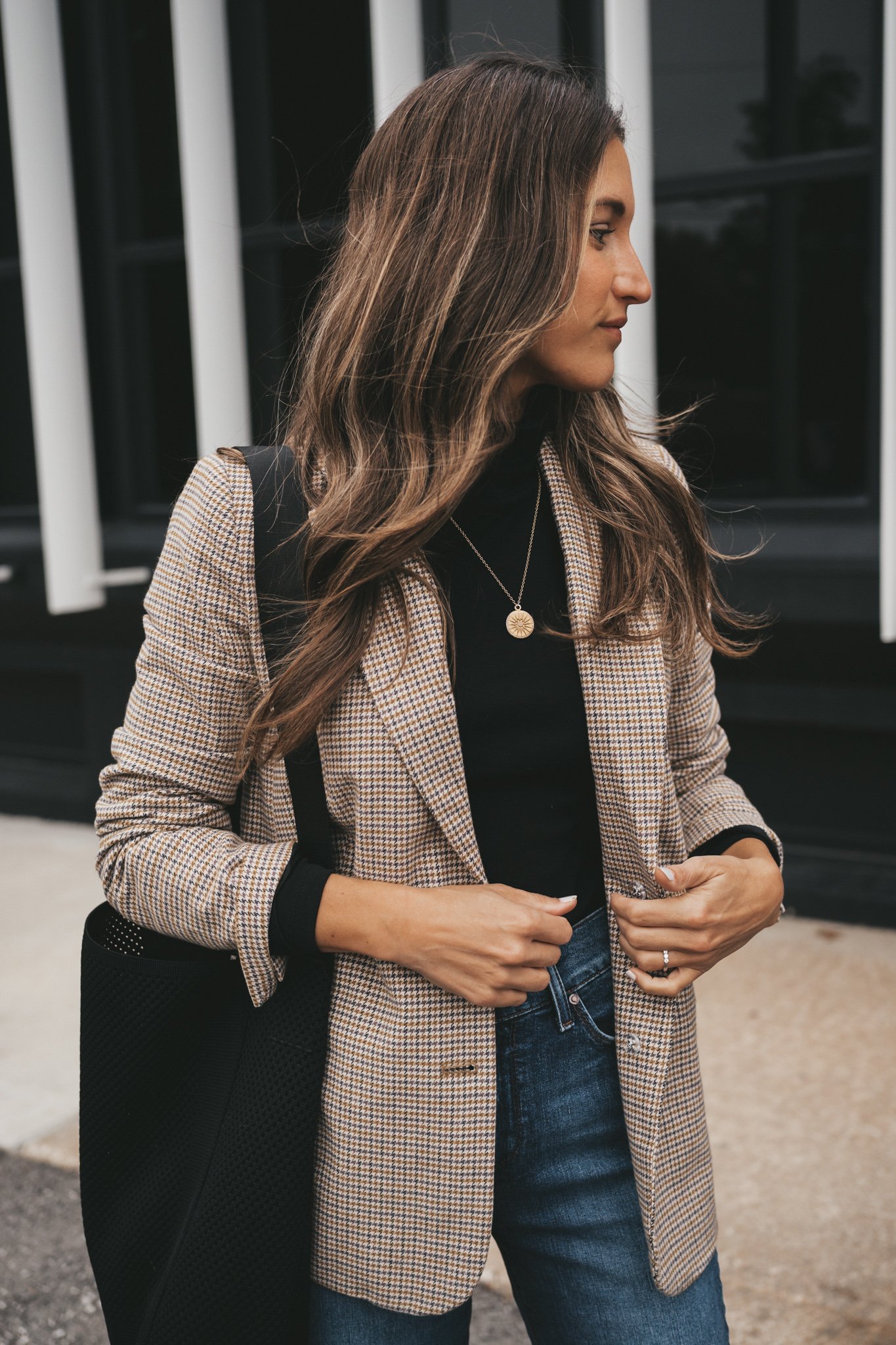 a black turtleneck outfit with a plaid blazer, dark wash denim, and a black bag