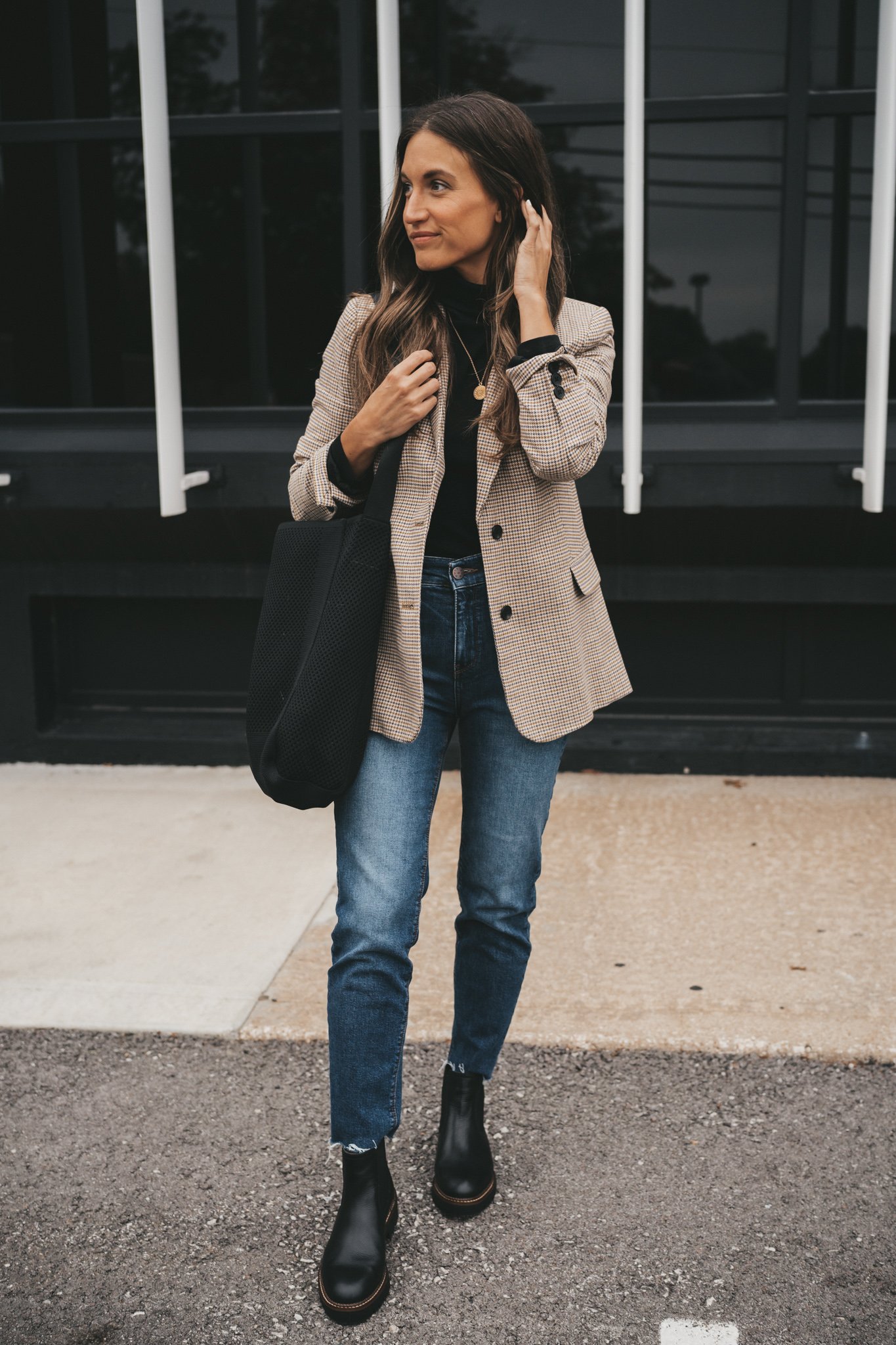 ashley wearing a black turtleneck under a plaid blazer, medium wash mom jeans, and black lug sole boots standing in front of a black building with large windows