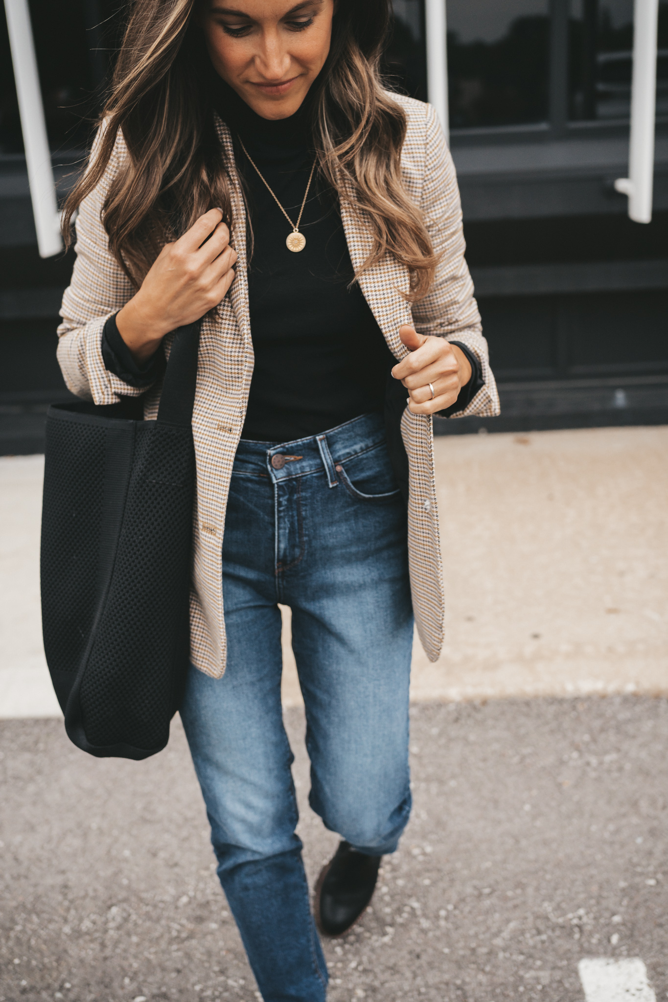 ashley wearing a black turtleneck under a plaid blazer, medium wash mom jeans, and black lug sole boots sitting on cement stairs with a black metal railing