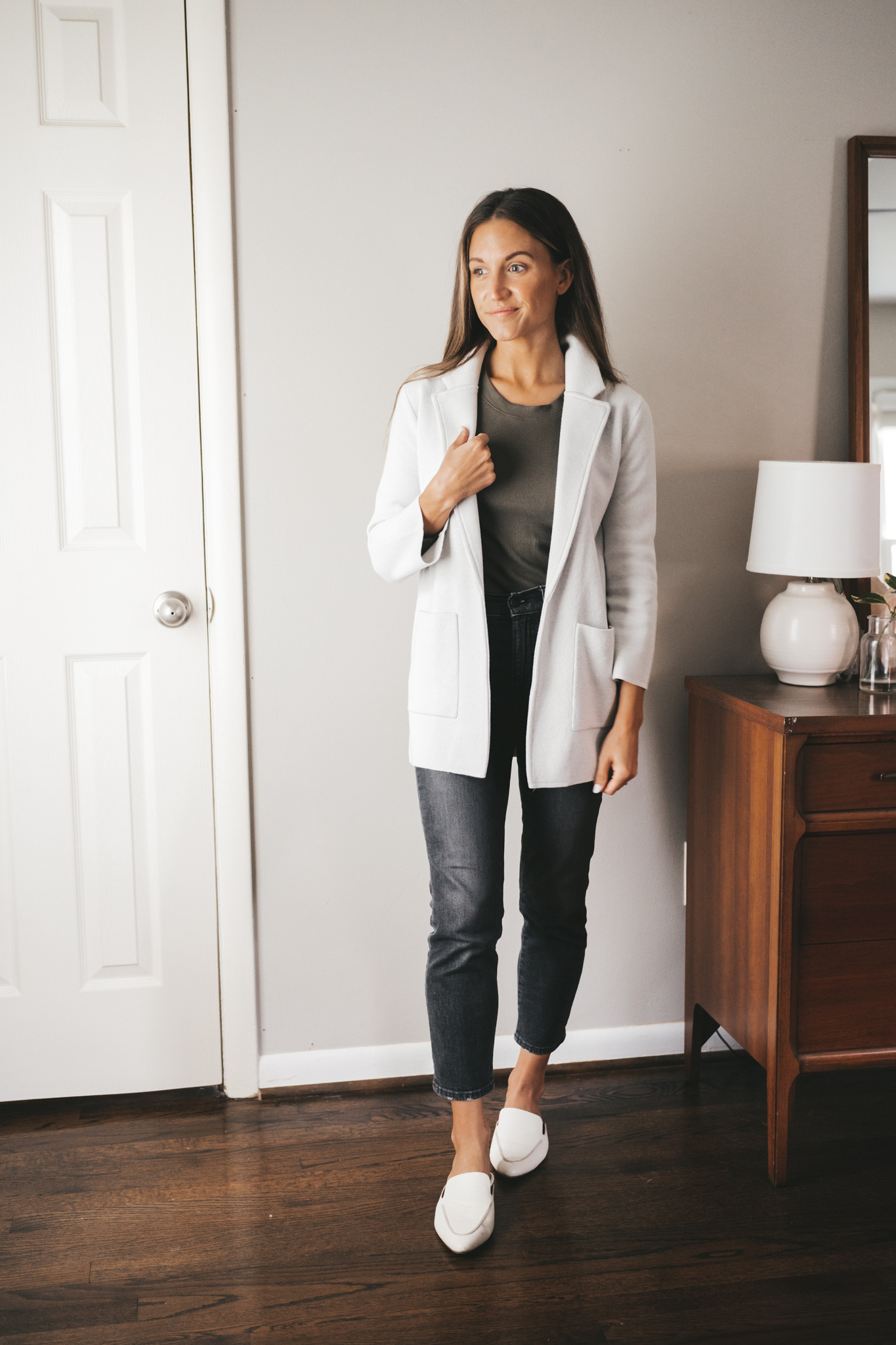 ashley wearing an olive green long sleeved tee under a light gray sweater blazer, washed black cropped jeans, and white mules