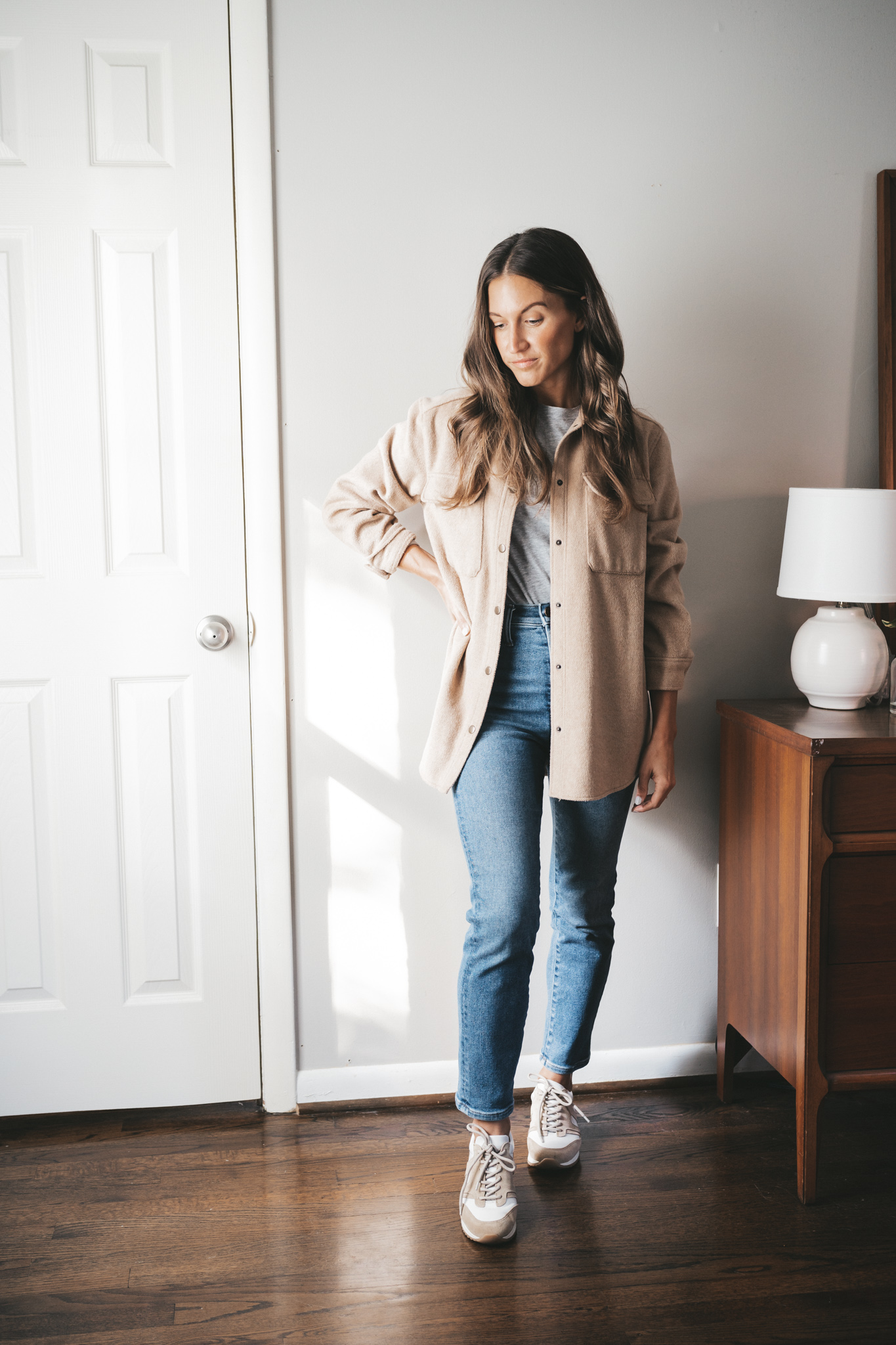 ashley wearing a gray long sleeved tee under a tan colored shacket with medium wash denim and white and tan sneakers