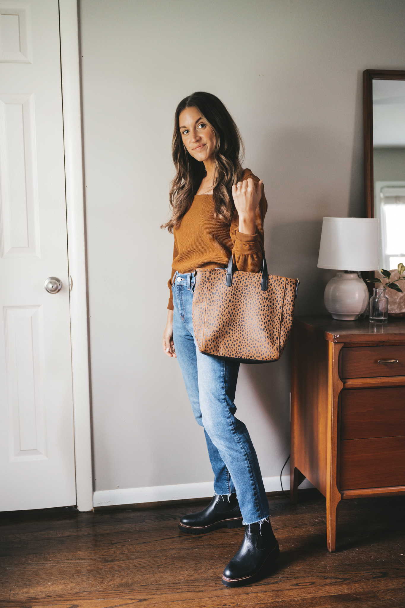 ashley wearing a brown square neck top tucked into to medium wash mom jeans with black lug sole boots holding a leopard print tote bag