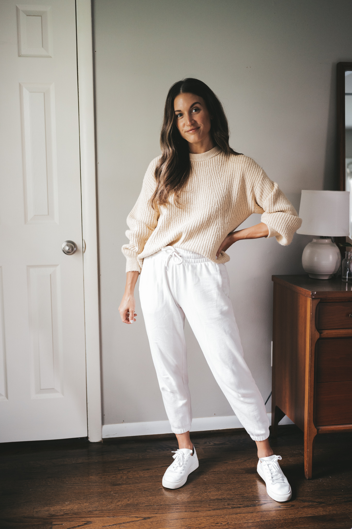 ashley wearing a cream colored sweater, white joggers, and white sneakers