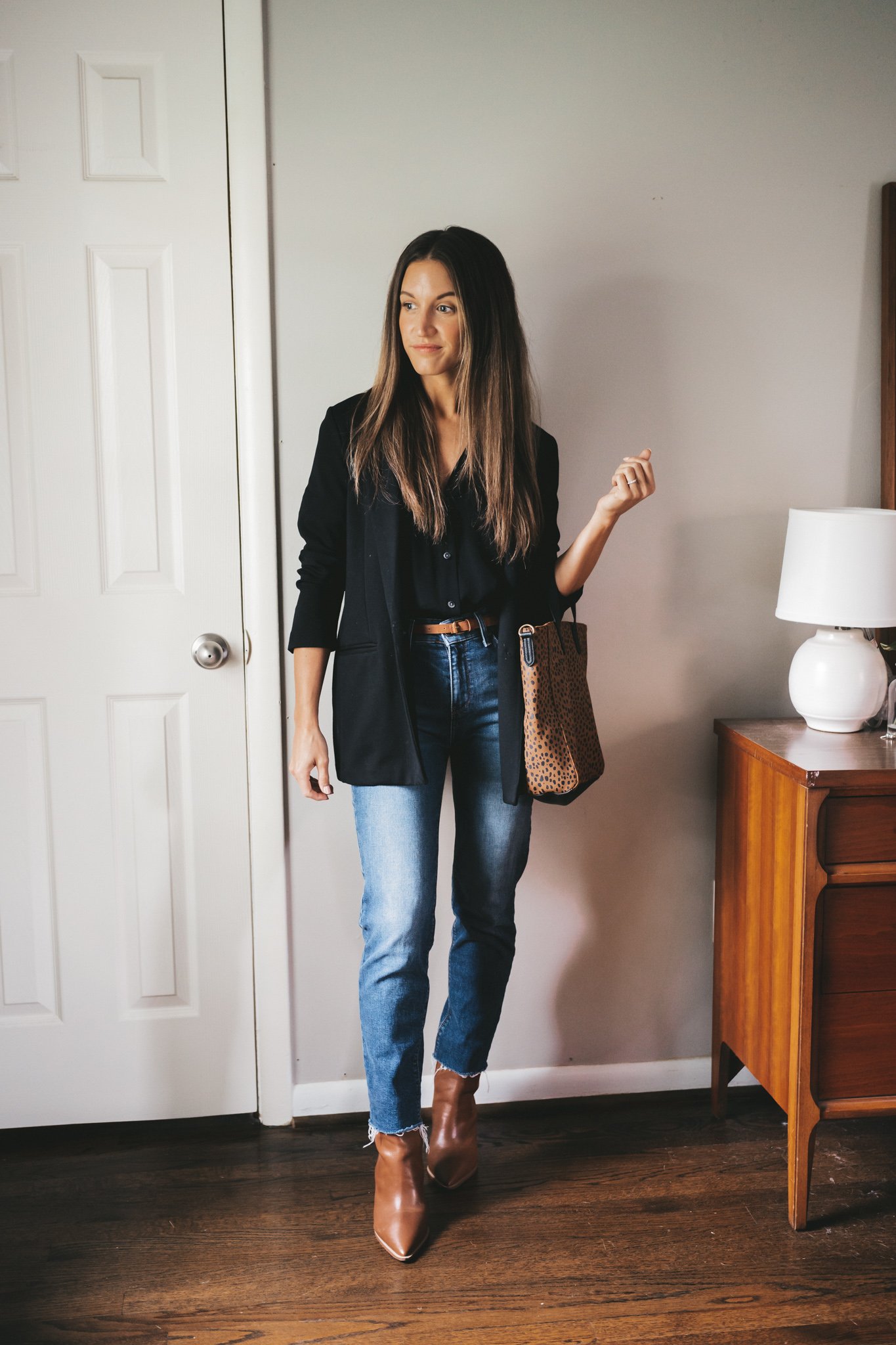 ashley wearing a black button down, black blazer, mid-wash mom jeans, brown heeled boots, and a leopard print tote bag