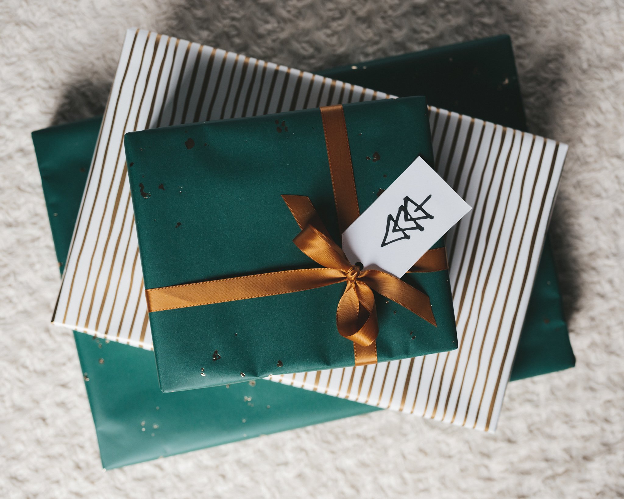 a picture of christmas gifts from above wrapped in emerald green and gold foil wrapping and tied with gold ribbon with a white tag