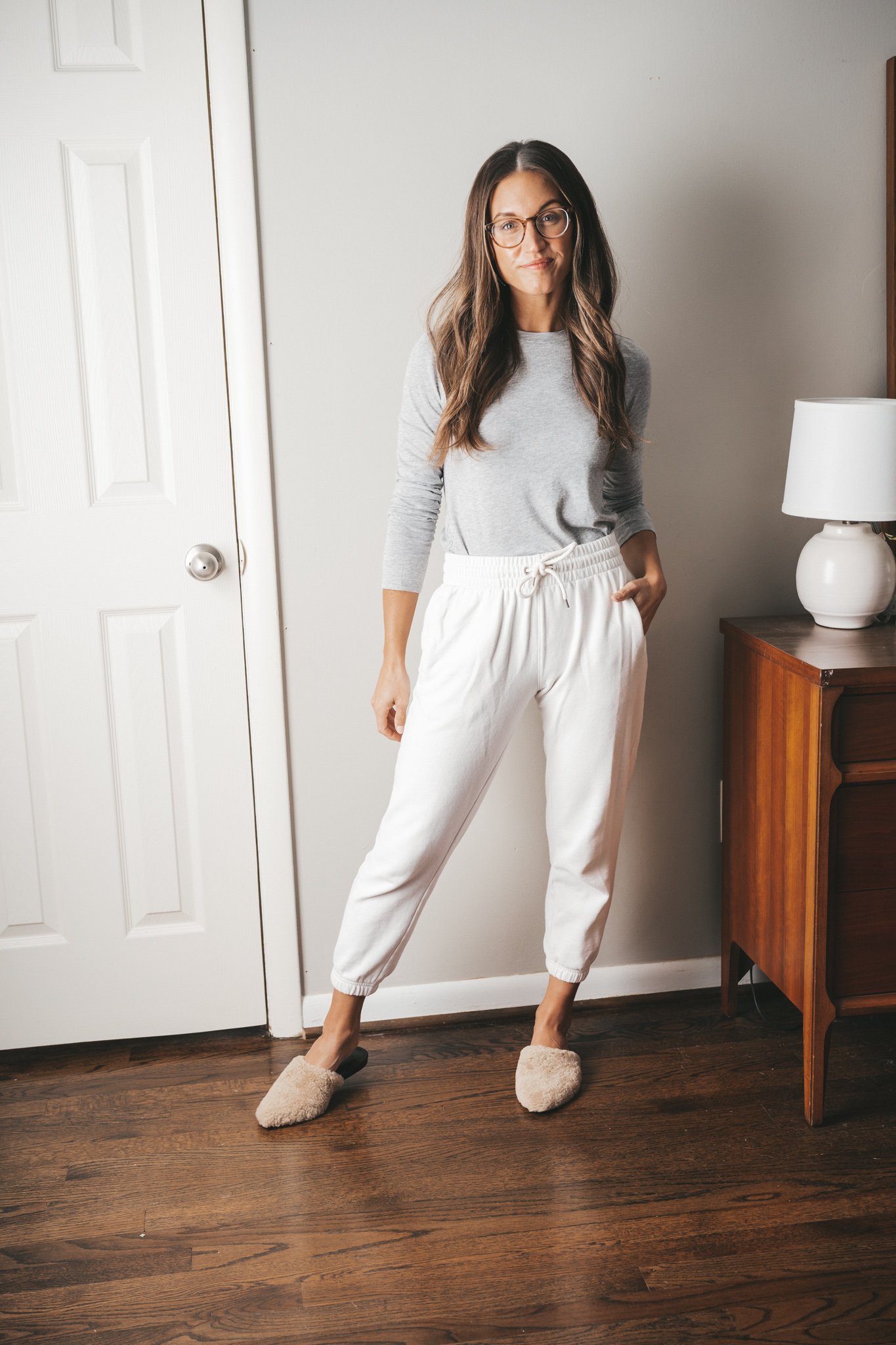 ashley wearing a long sleeved gray tee, white joggers, and tan shearling mules with glasses