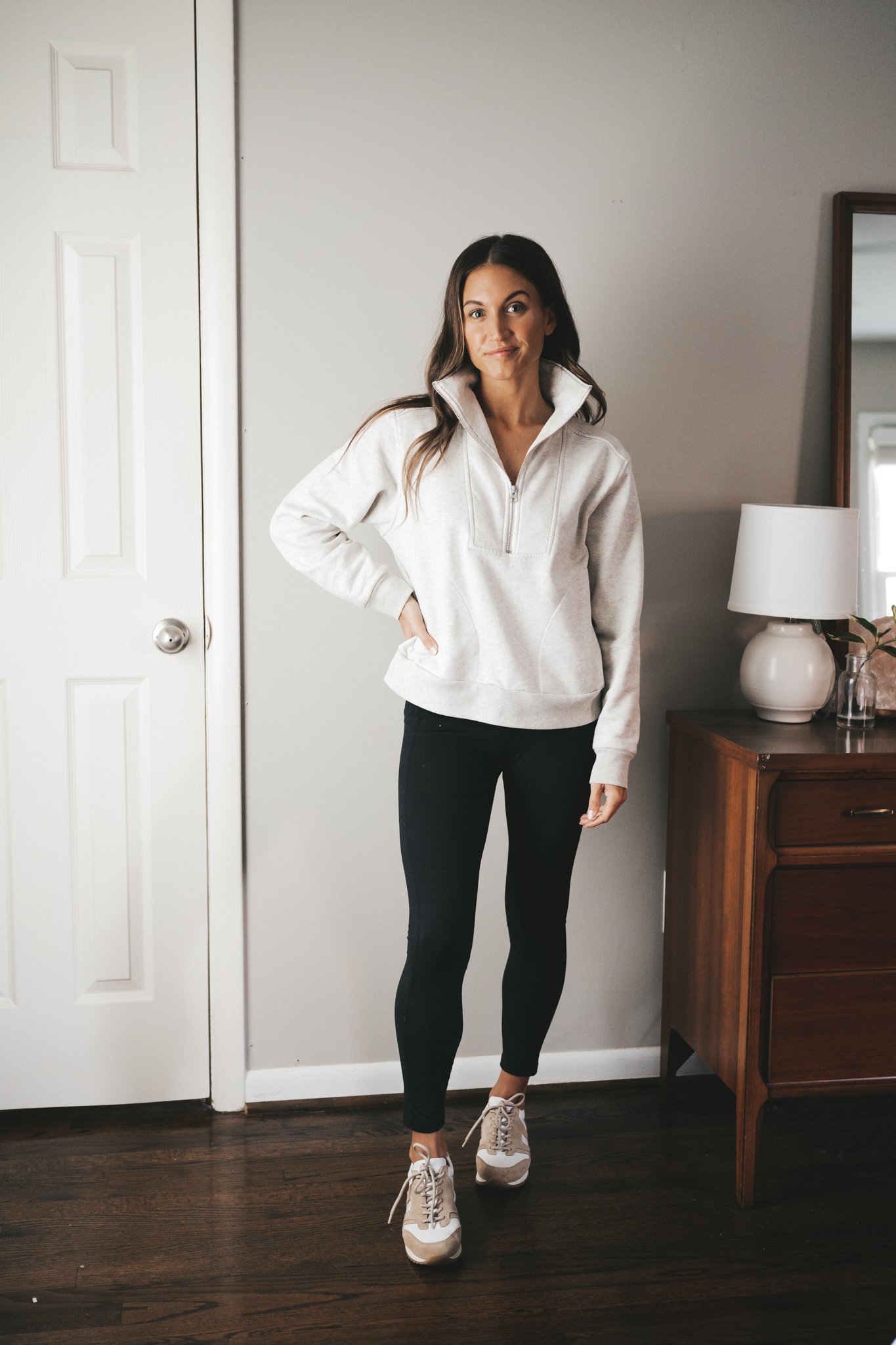 ashley wearing a gray half zip sweatshirt, black leggings, and white sneakers