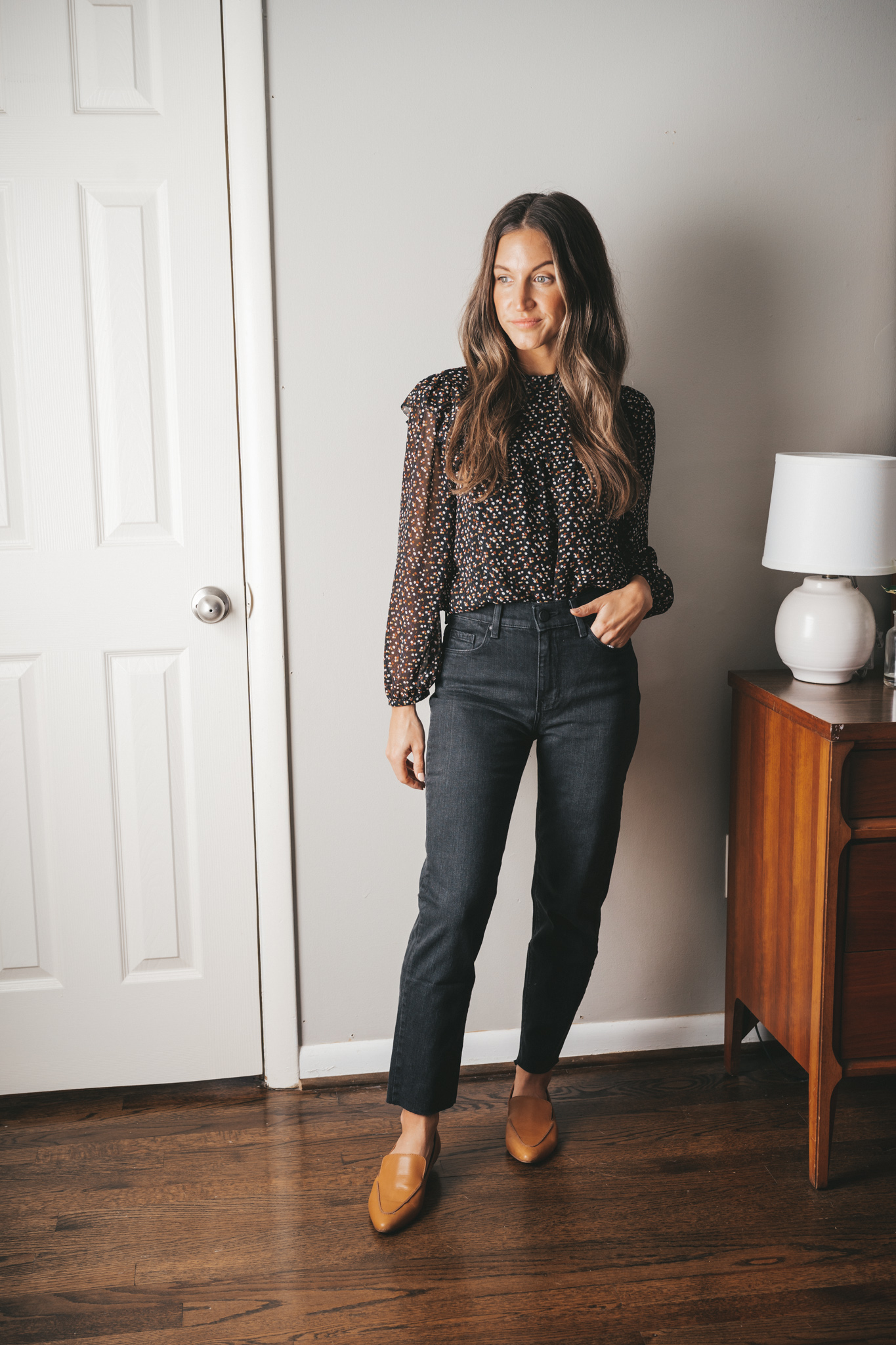 ashley wearing a black floral blouse, black mom jeans, and cognac loafers