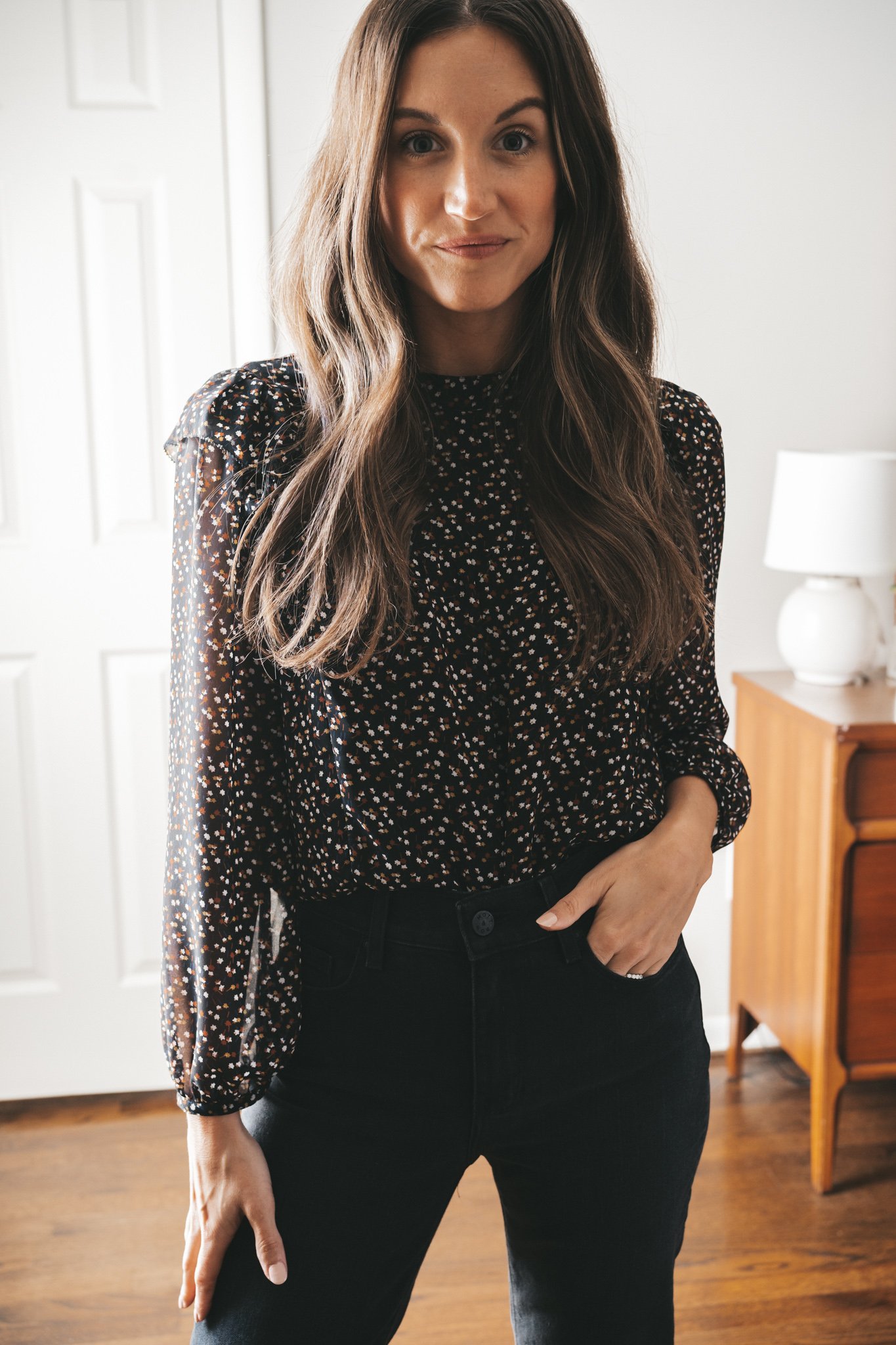 ashley wearing a black floral blouse, black mom jeans, and cognac loafers