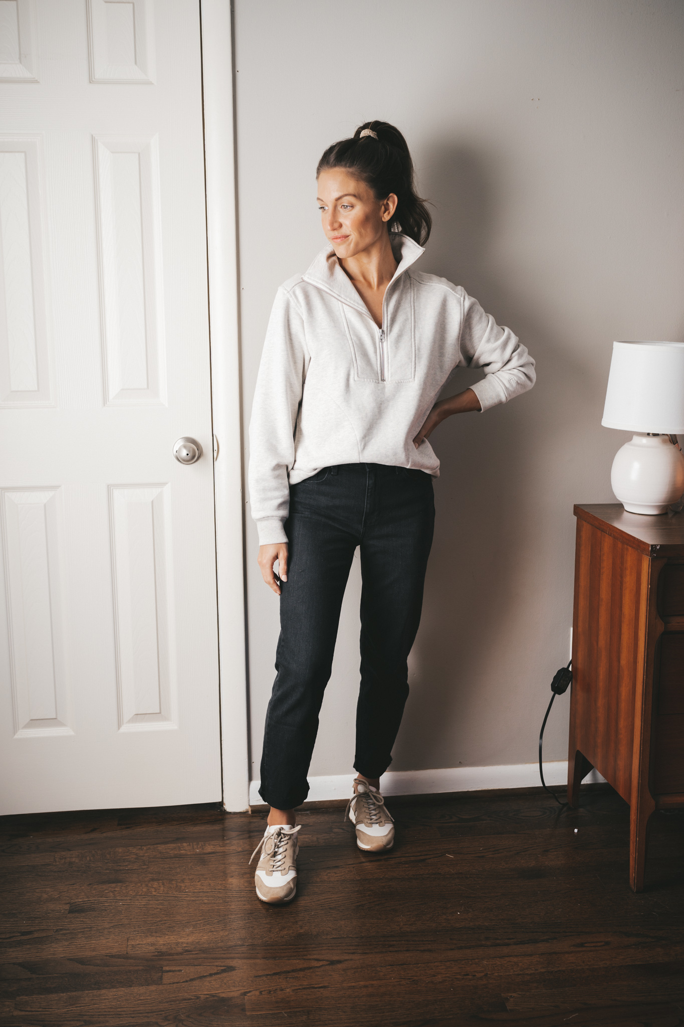 ashley wearing a gray half-zip sweatshirt, black mom jeans, and white sneakers with hair in a high pony
