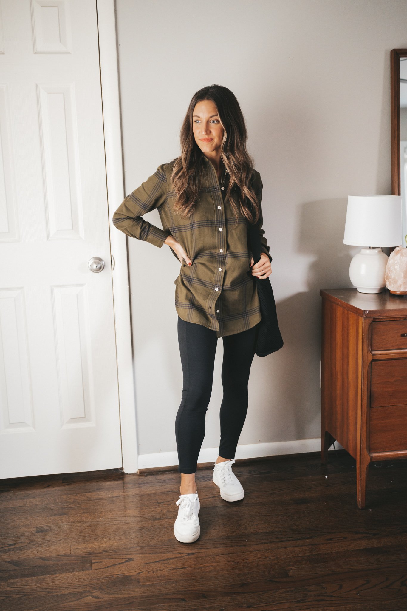 ashley wearing a black and green plaid flannel, black leggings, and white sneakers with a black tote bag over the shoulder