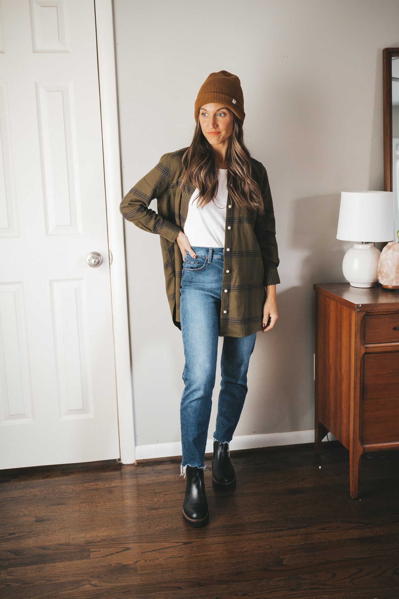 ashley wearing a green and black plaid flannel unbuttoned with a white tank, mid-wash mom jeans, and black lug sole chelsea boots with a brown beanie
