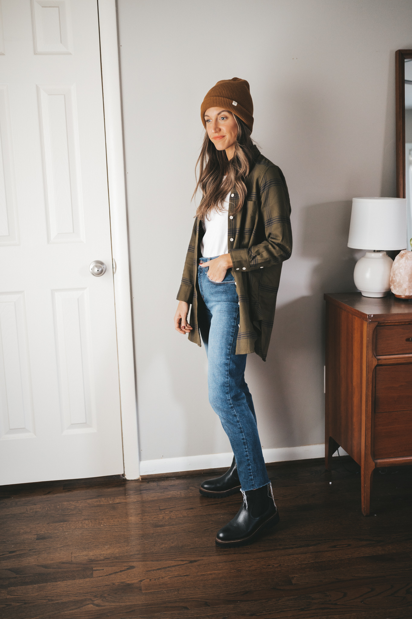 ashley wearing a green and black plaid flannel unbuttoned with a white tank, mid-wash mom jeans, and black lug sole chelsea boots with a brown beanie