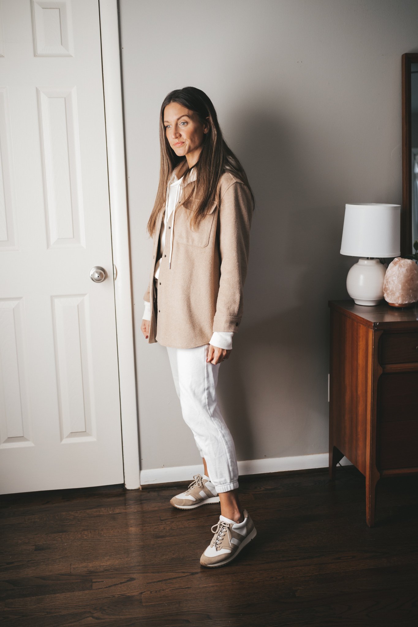 ashley wearing a cream colored hoodie under a tan shacket, white joggers, and white and tan leather sneakers