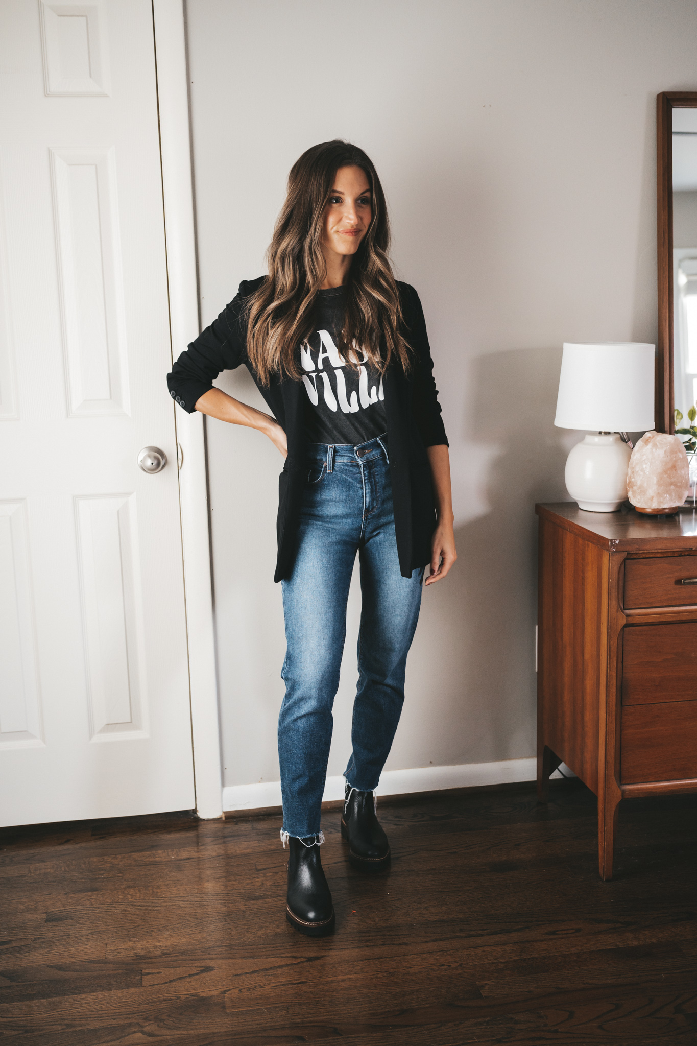ashley wearing a black graphic tee that reads "Nashville" in white under a black blazer, mid-wash denim, and black lug-sole boots