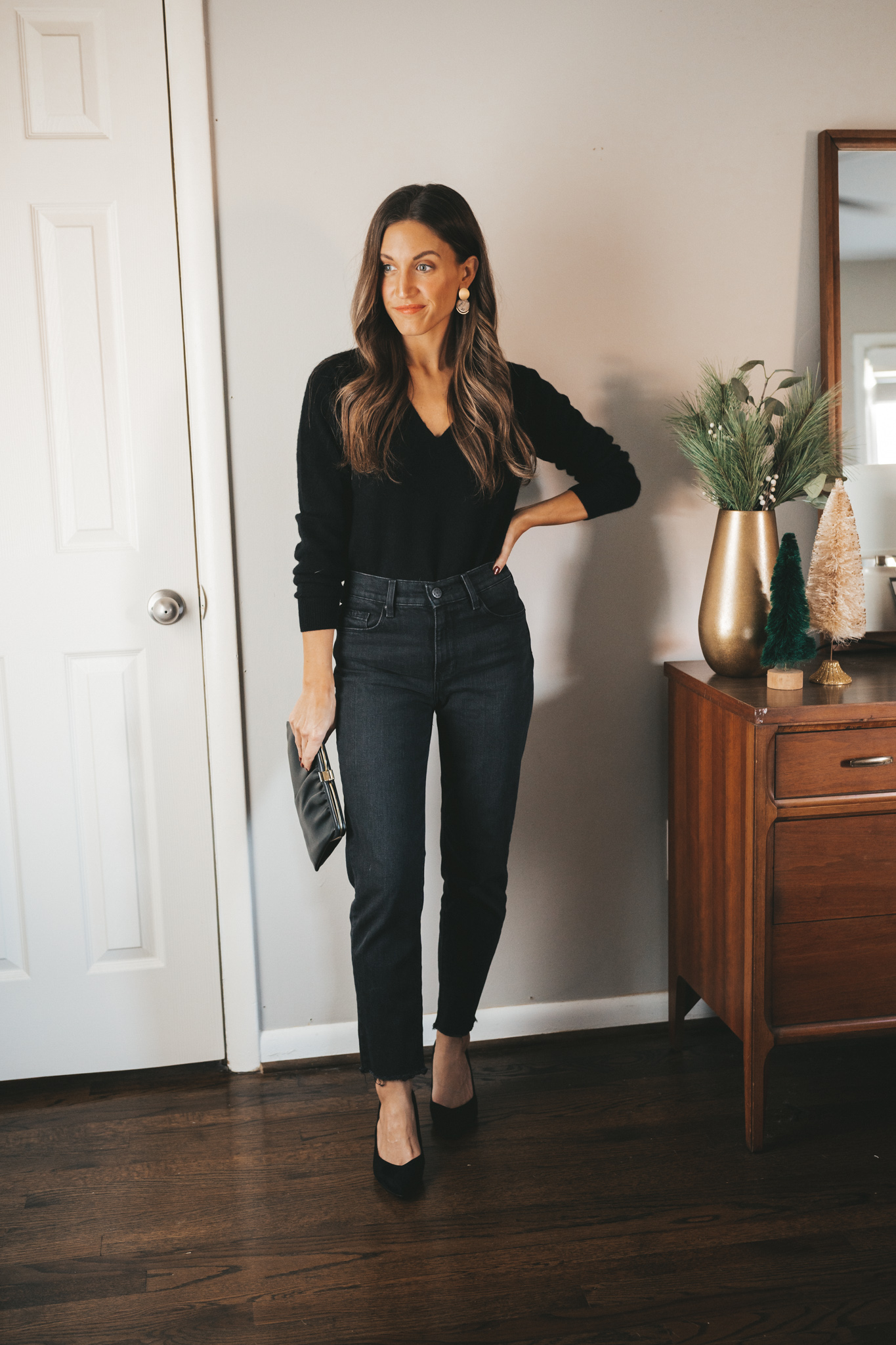 ashley wearing a v-neck black cashmere sweater, black denim, black block heel pumps, and a black vintage clutch. 