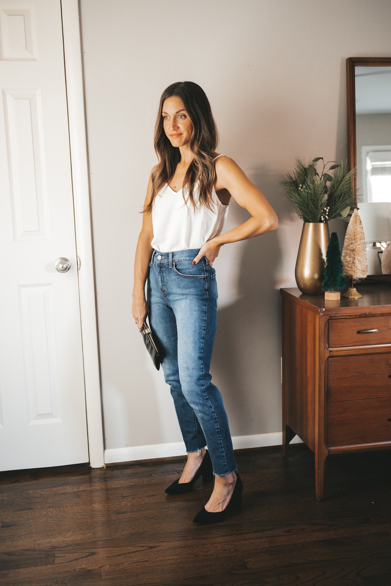 ashley wearing a white silk camisole, mid-wash denim, black block heel pumps, and a vintage black clutch