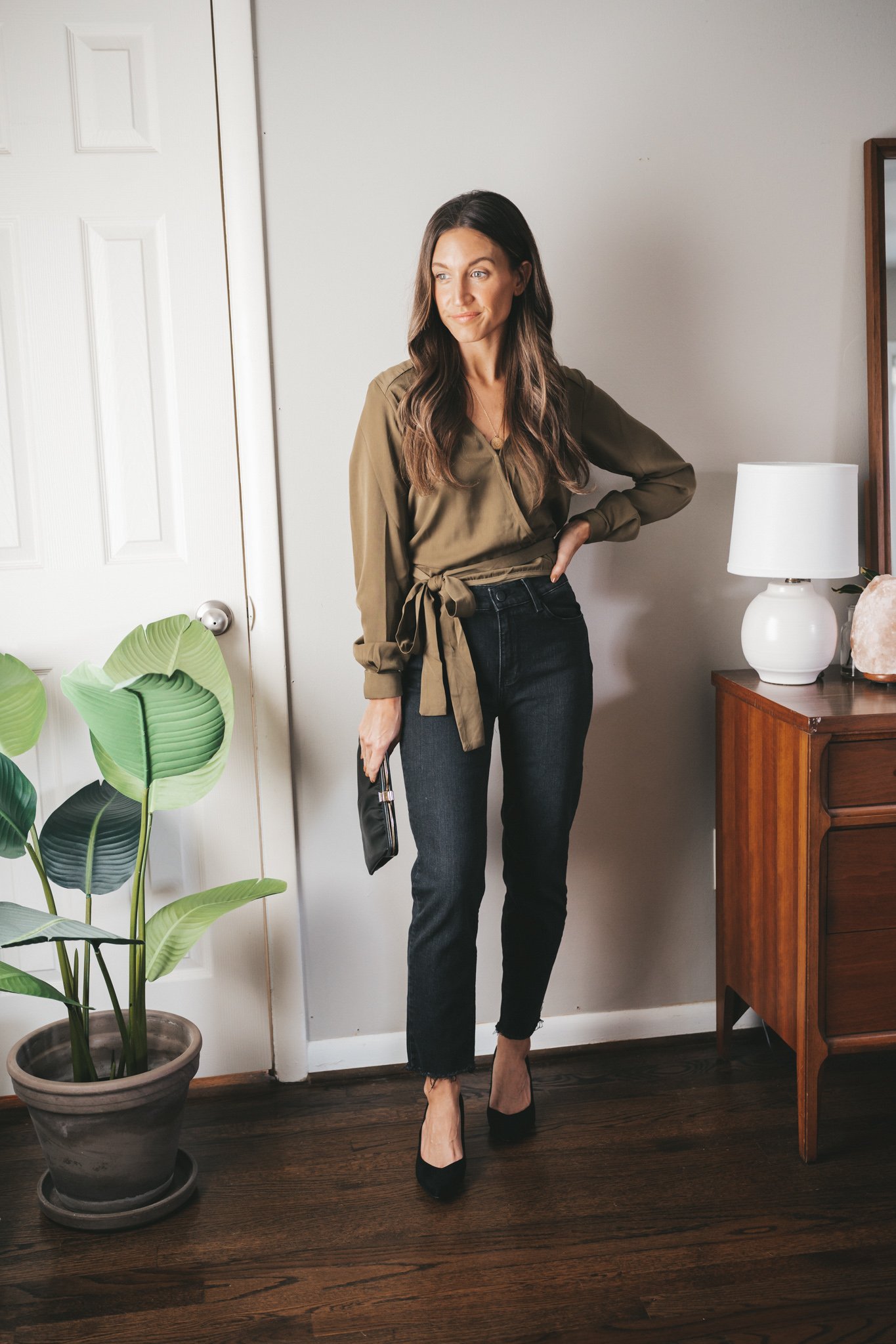 ashley wearing an olive green wrap top, black denim, black heels, and a black clutch