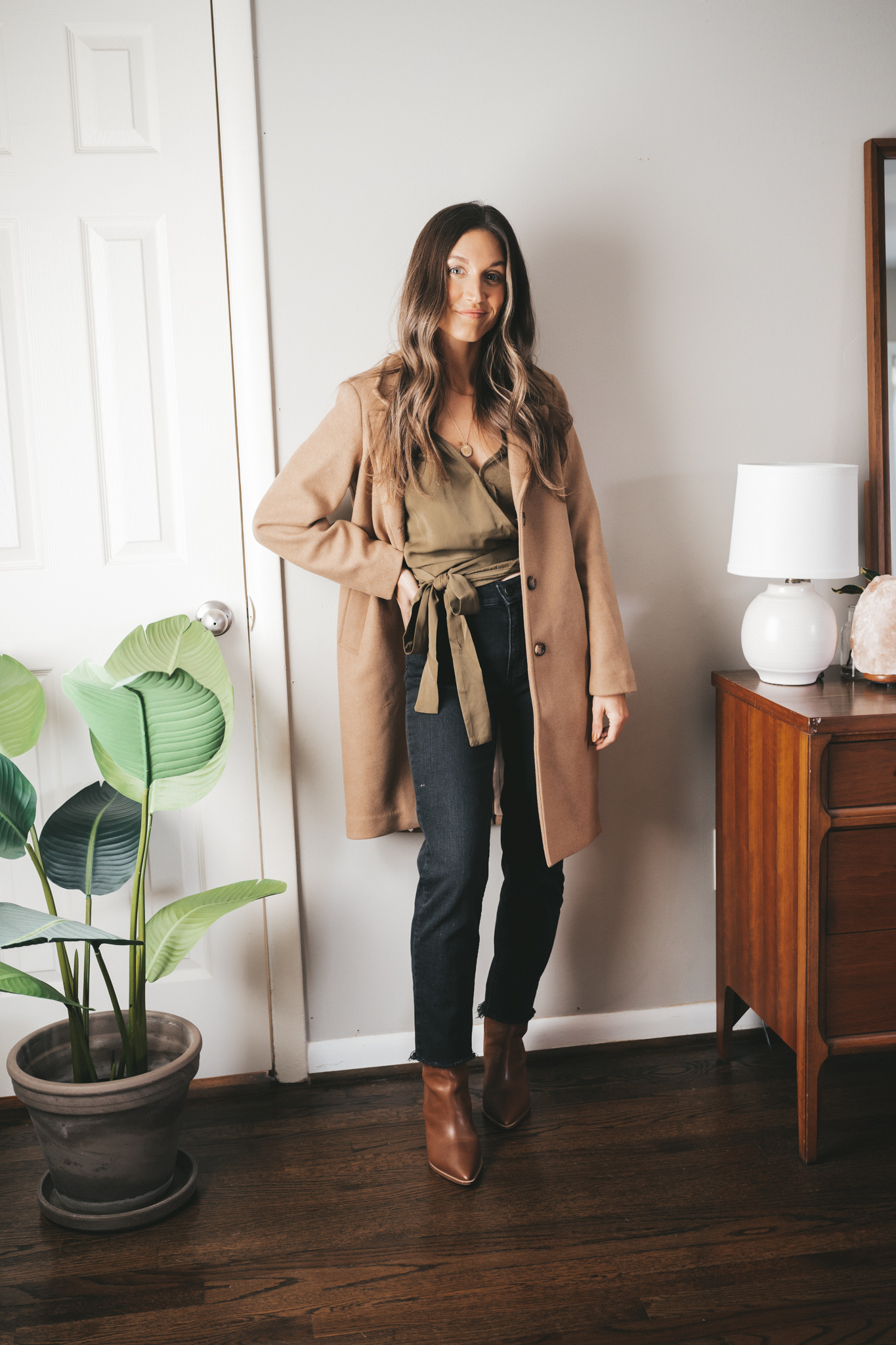 ashley wearing an olive green wrap under a camel coat, black denim, and brown ankle boots